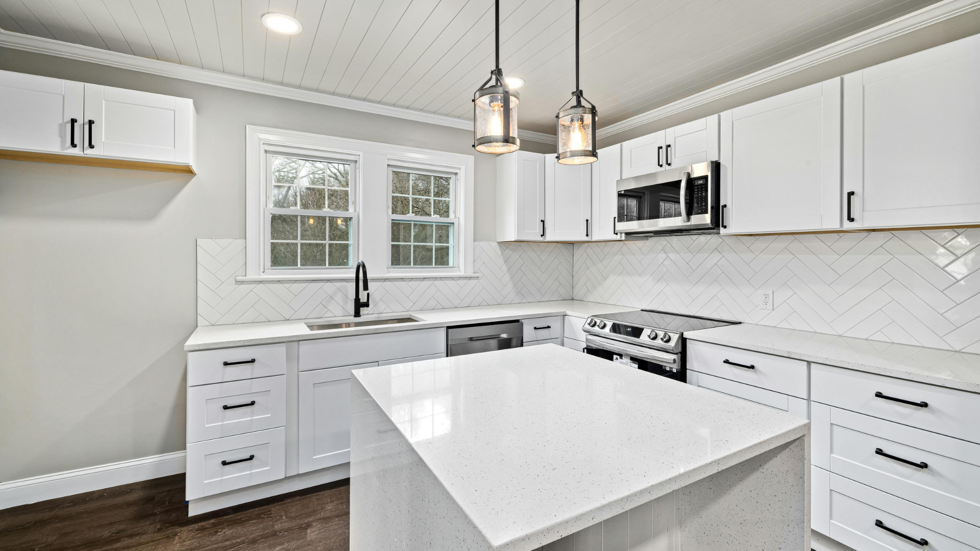 White kitchen with island, cabinets, appliances, windows, and pendant lights.