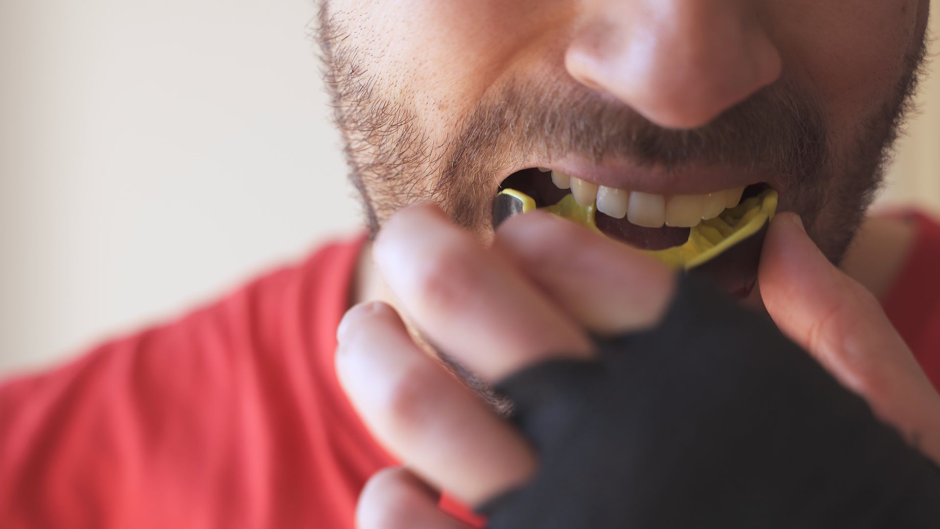 Close-up of a person biting a yellow strap while wearing black fingerless gloves and a red shirt