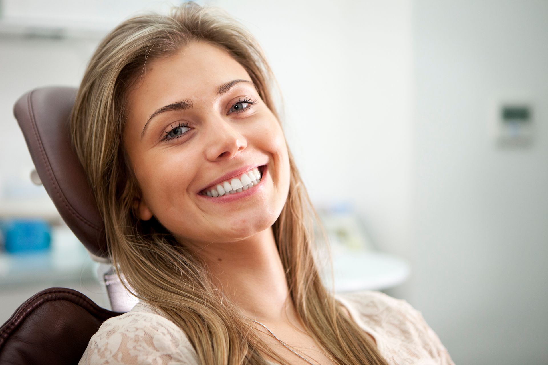 A woman is smiling while sitting in a dental chair.