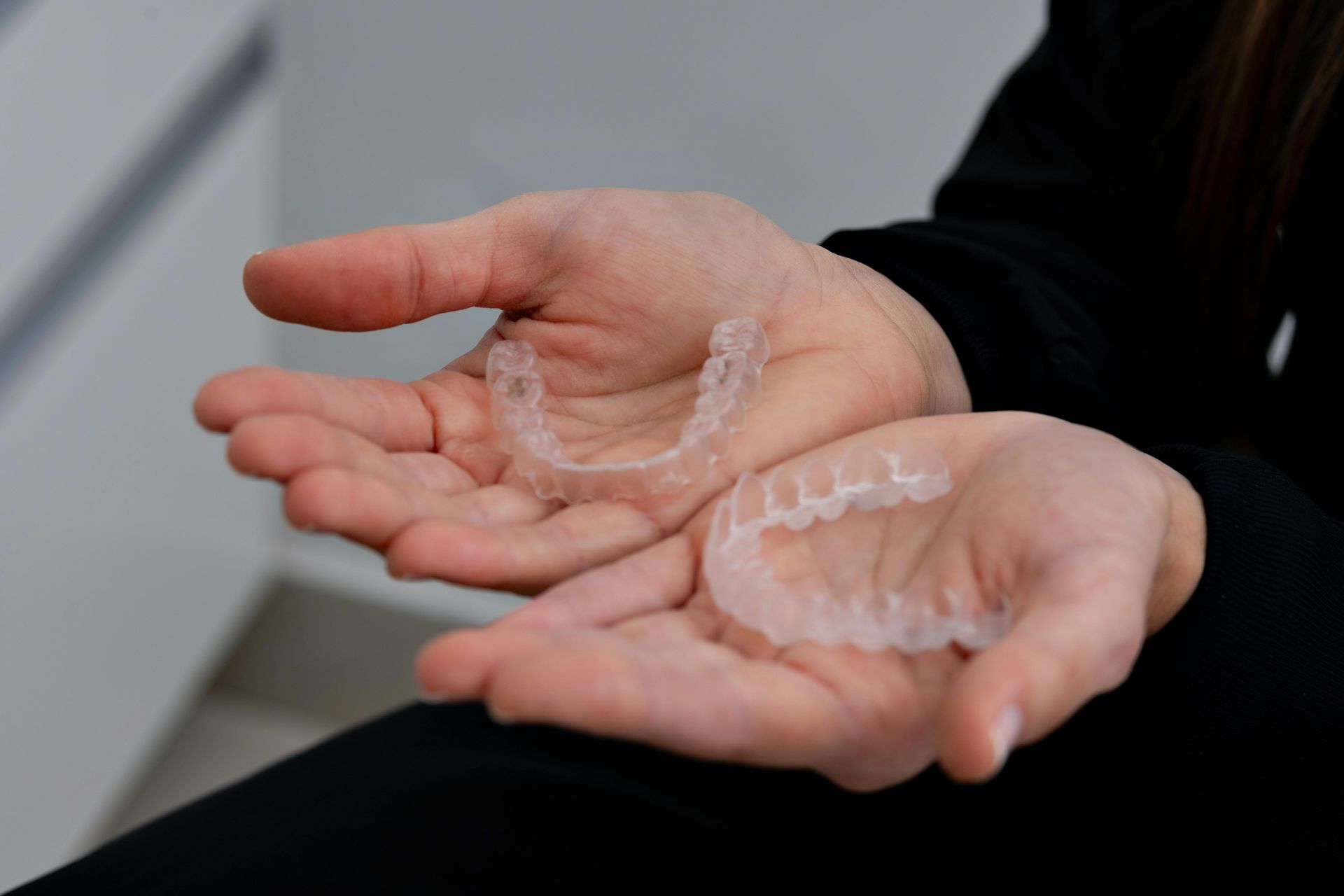 Two hands holding clear aligner trays over a dark background