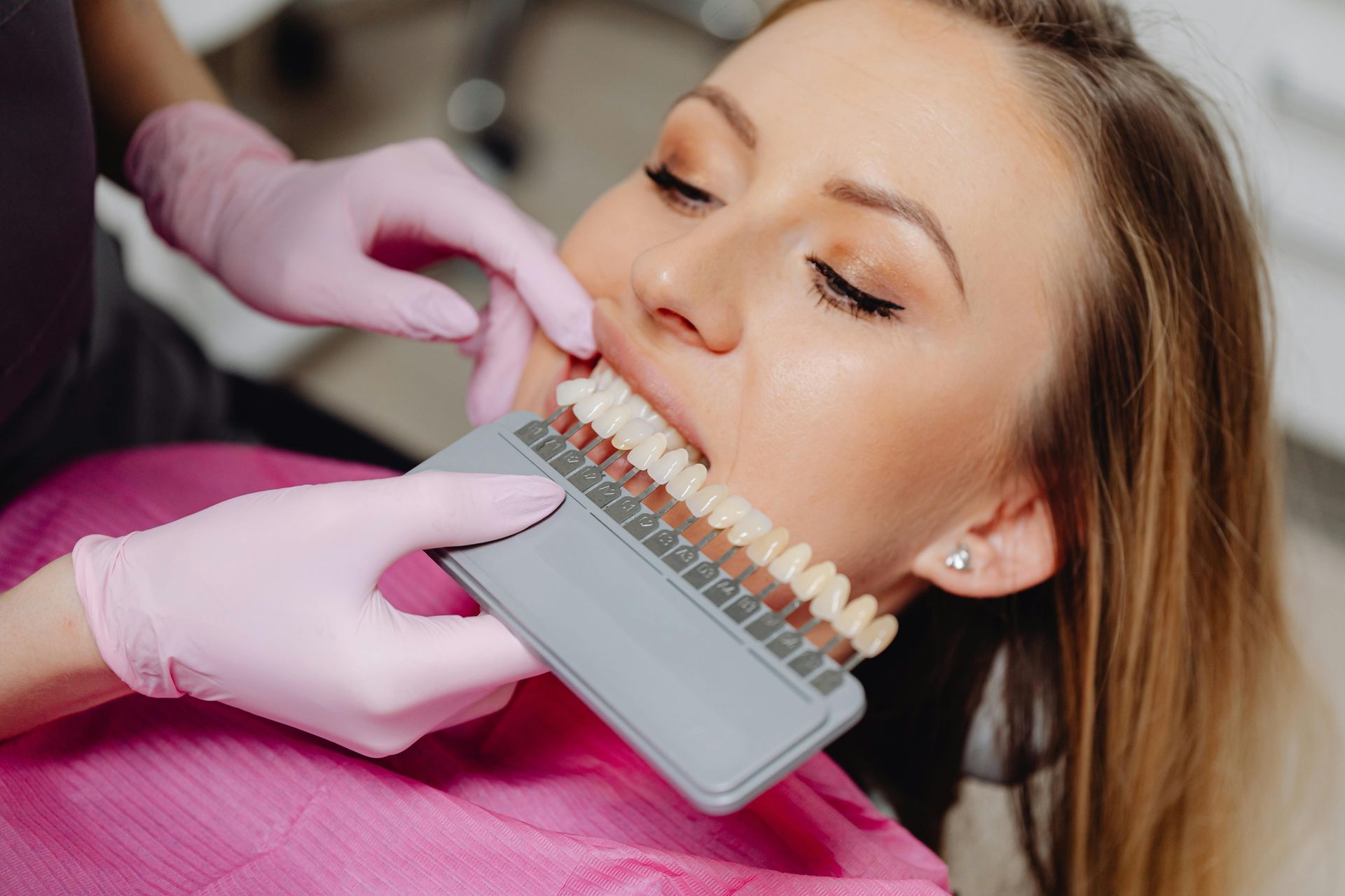 Dentist showing tooth shade options to a patient in pink gloves during a cosmetic consultation