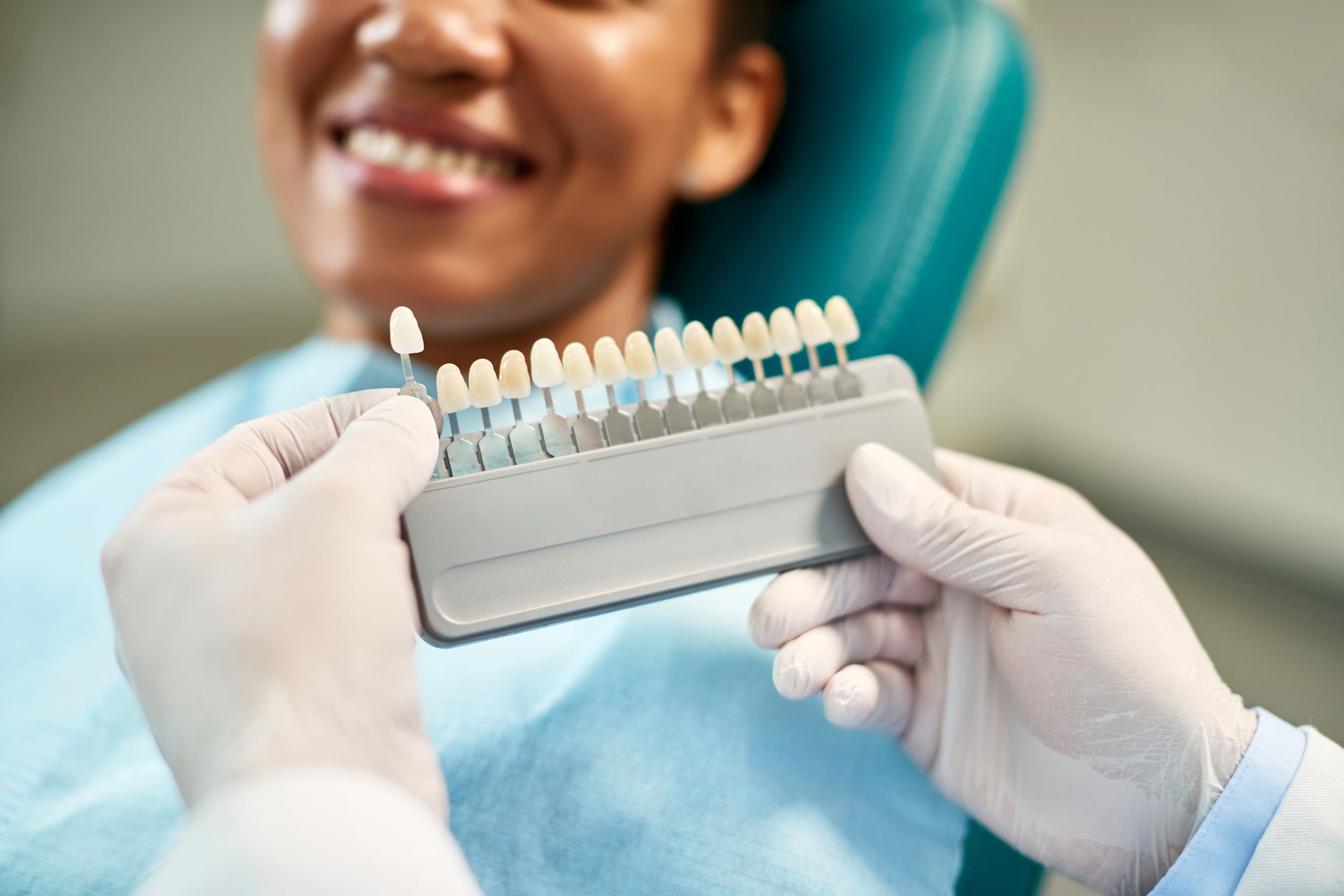 A dentist is holding a tooth color chart in front of a smiling woman