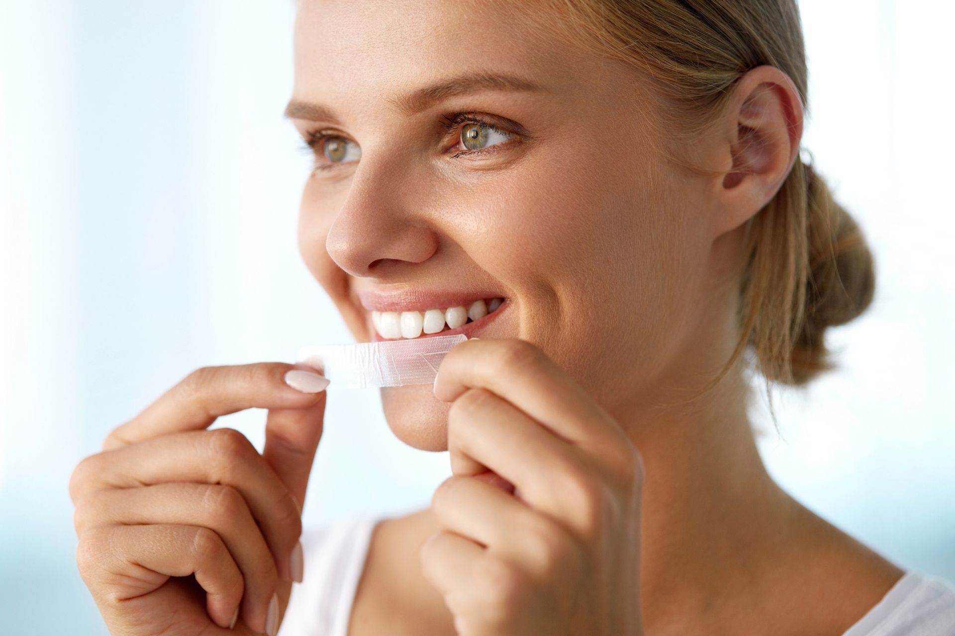 A woman is applying whitening strips to her teeth.