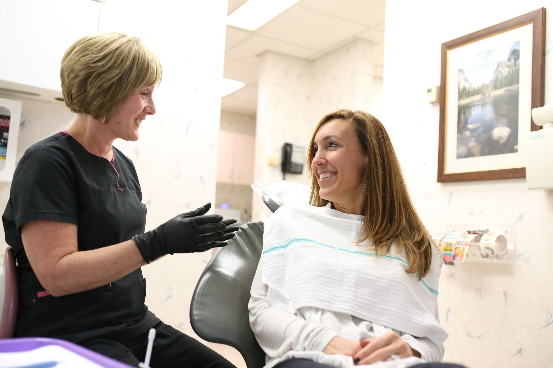 A woman is sitting in a dental chair talking to another woman