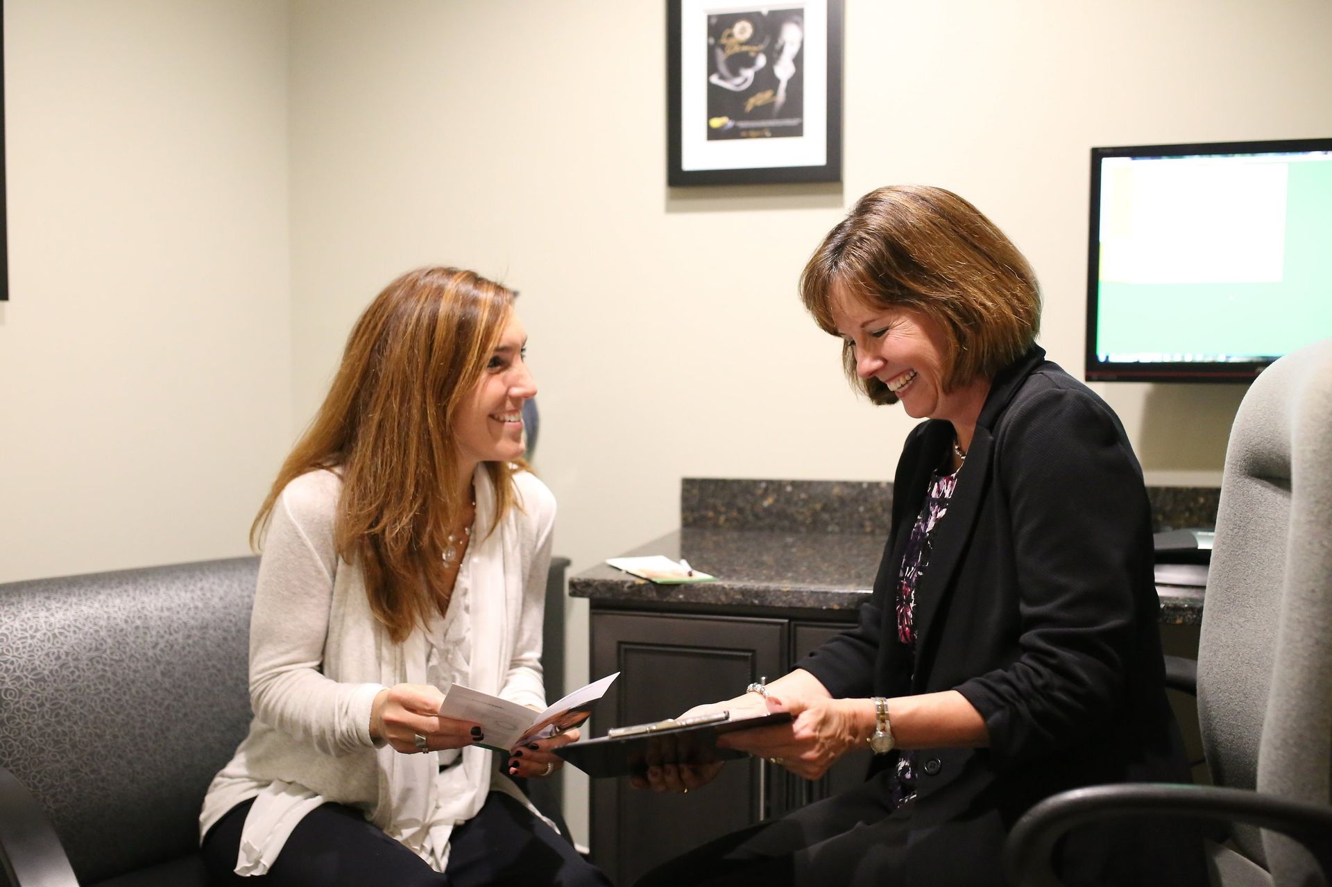 Two women are sitting on a couch looking at a clipboard