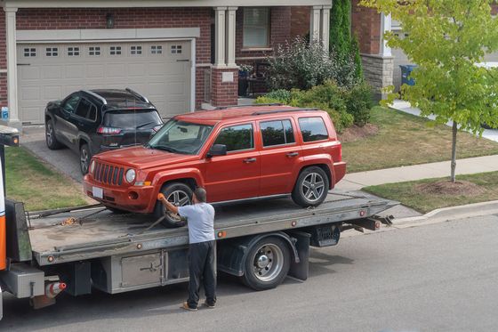 a red jeep is on the back of a flatbed truck