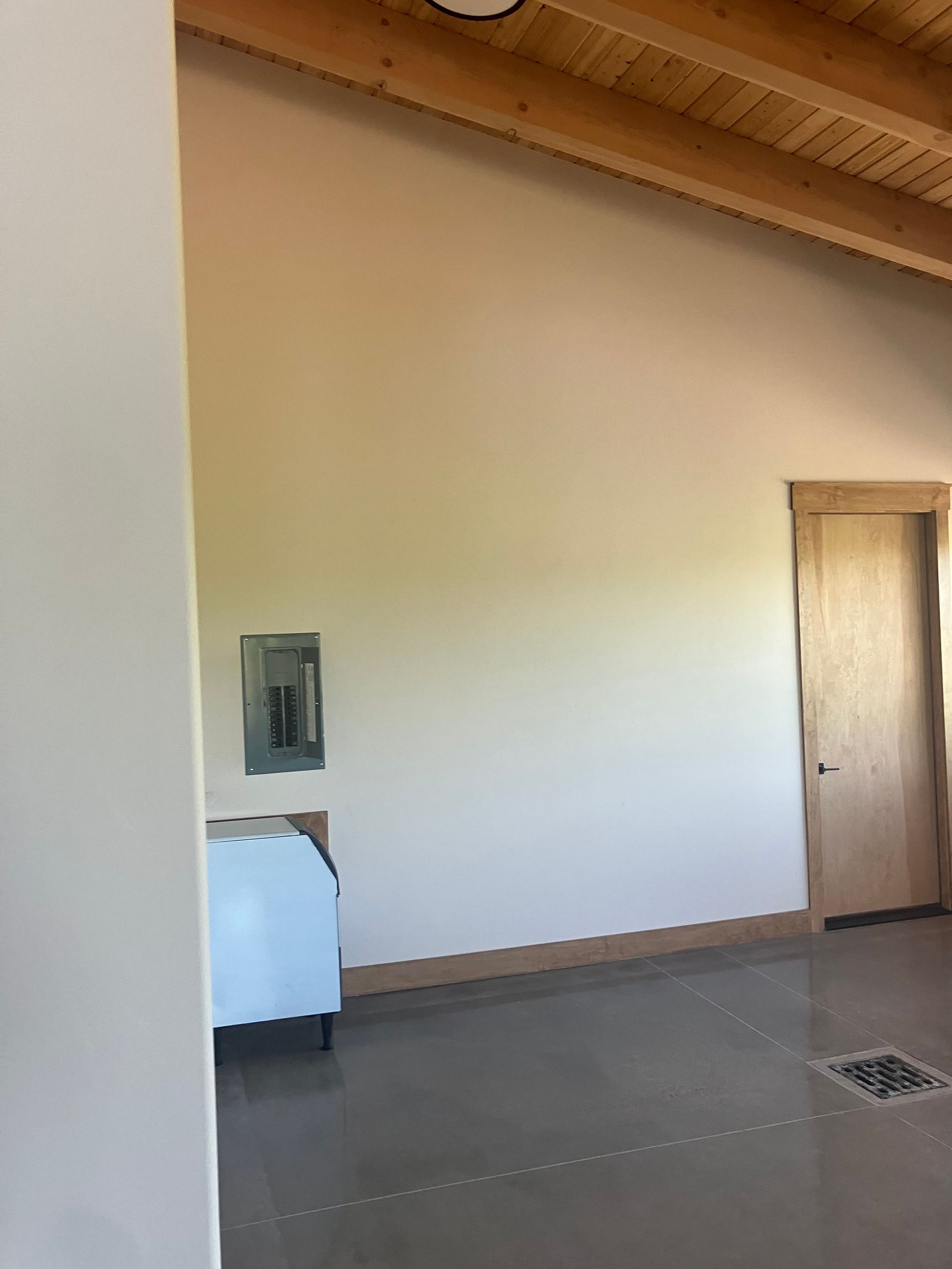 Room interior with a high, angled ceiling, concrete floor, door, and a bed.