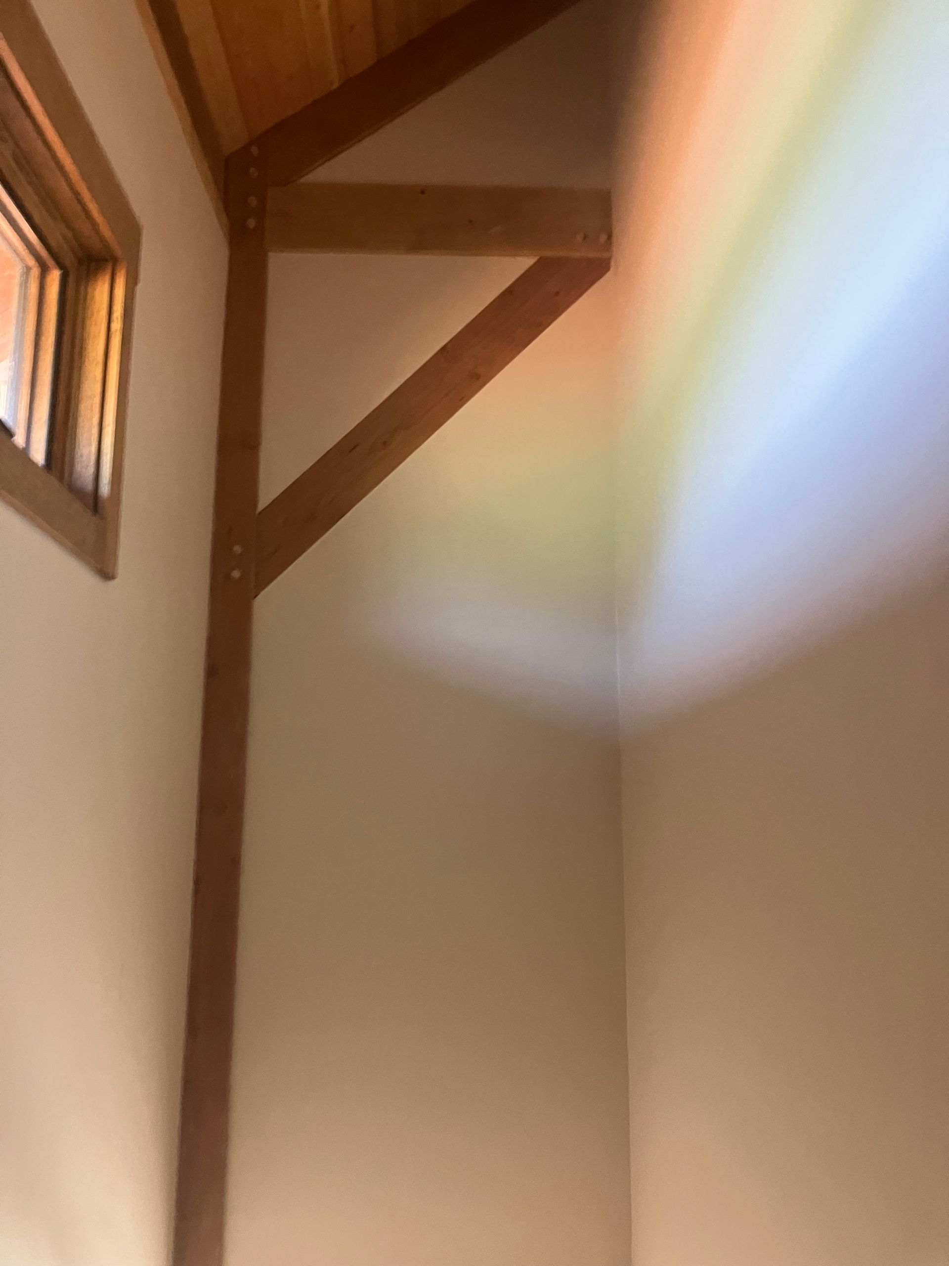 Wooden support beam in the corner of a room, illuminated by a rainbow of colors on a beige wall.