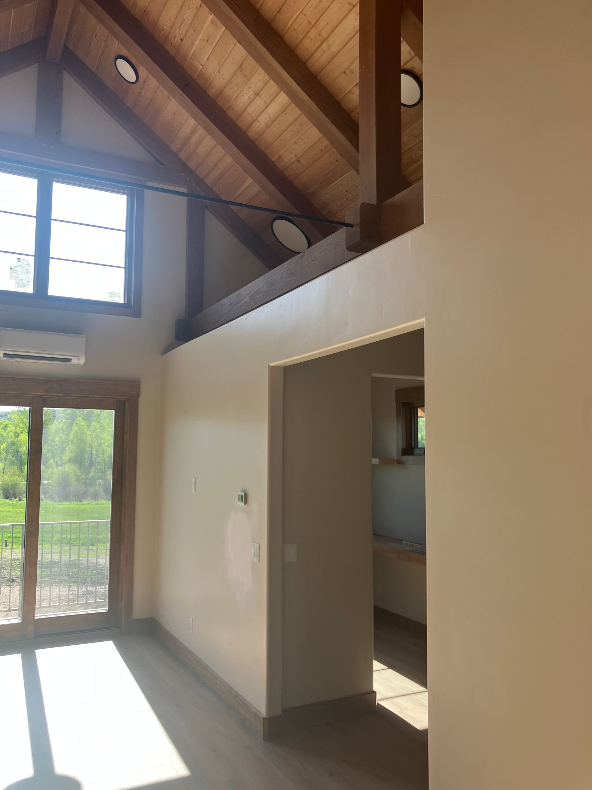 Interior view of a room with wood ceiling beams, a window, and an open doorway.
