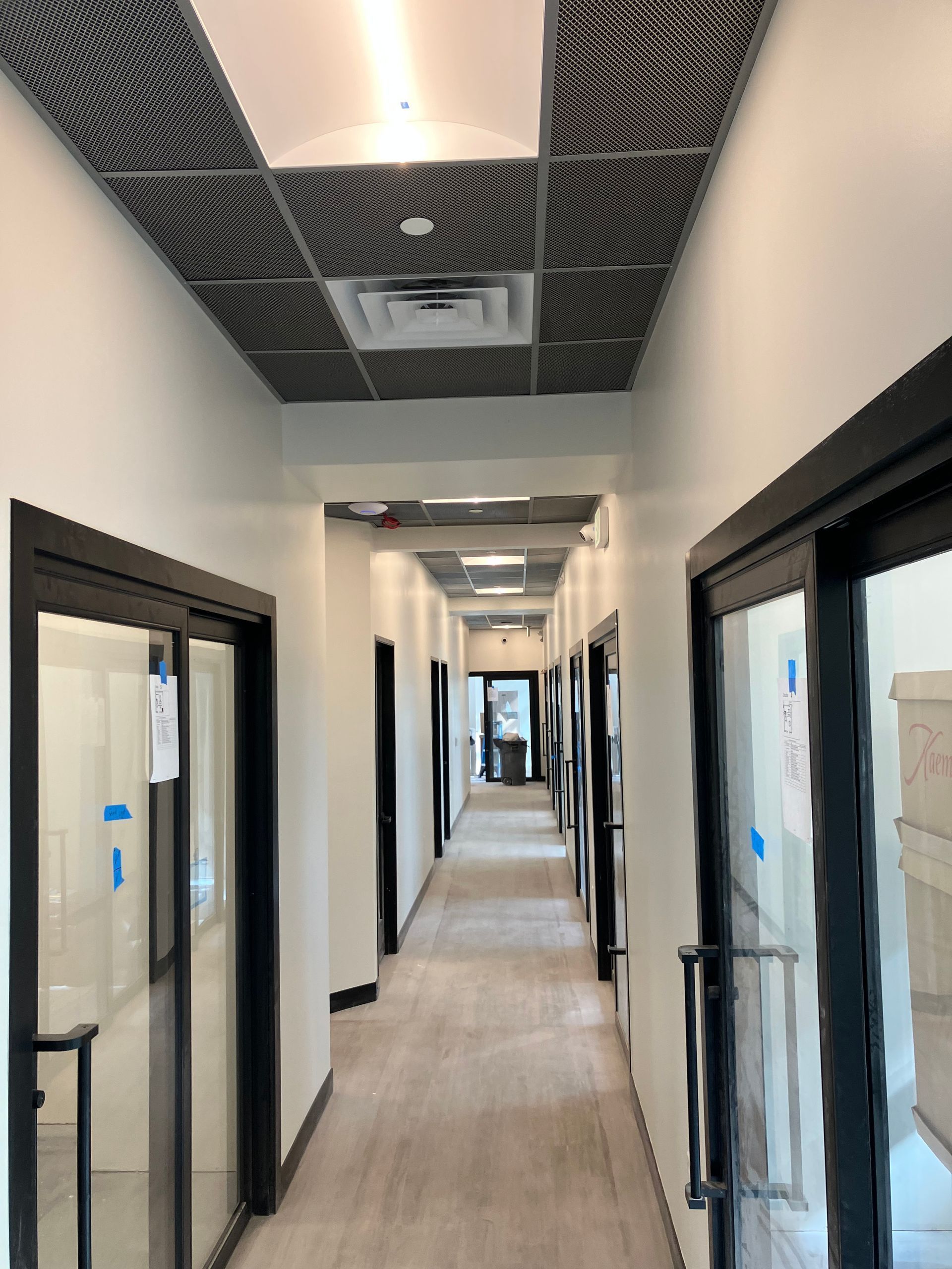 Hallway with several doors on both sides; a textured ceiling and light-colored floors.