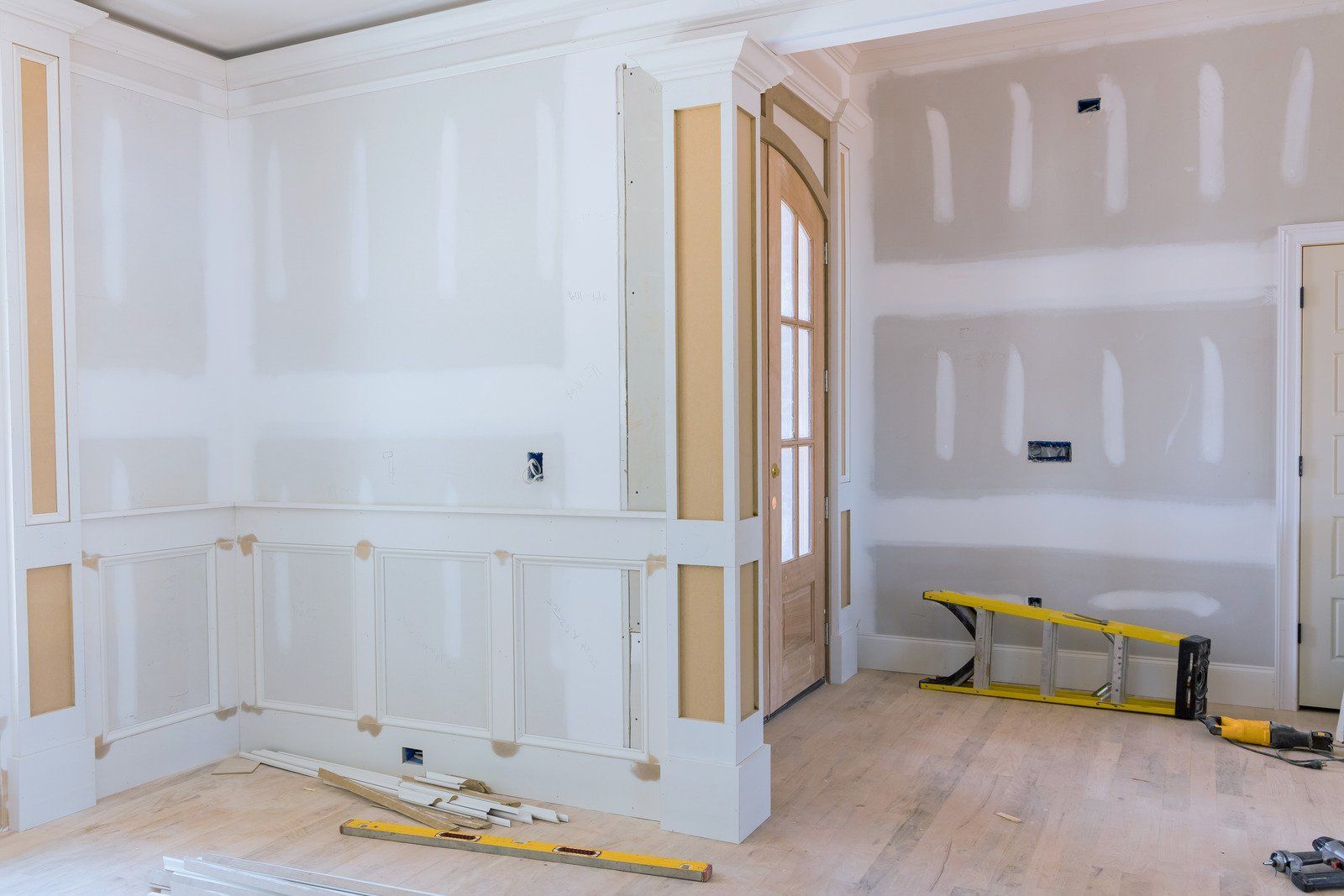 Interior room under construction, featuring drywall on walls, doorway, and tools on the floor.