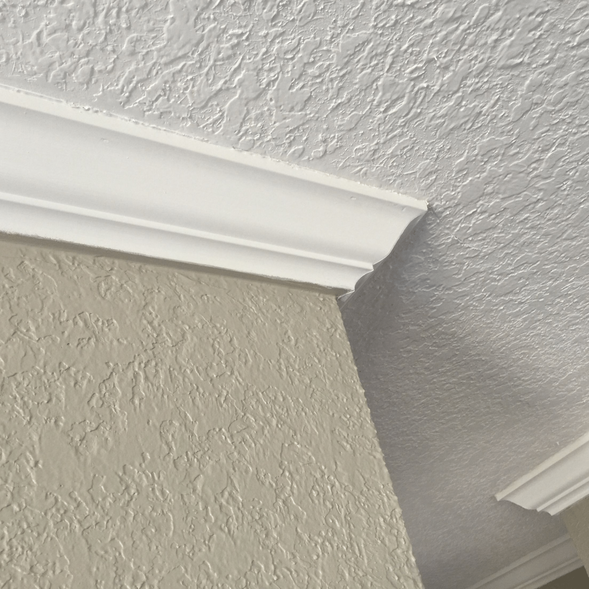White crown molding at the corner where a textured beige wall meets a textured white ceiling.