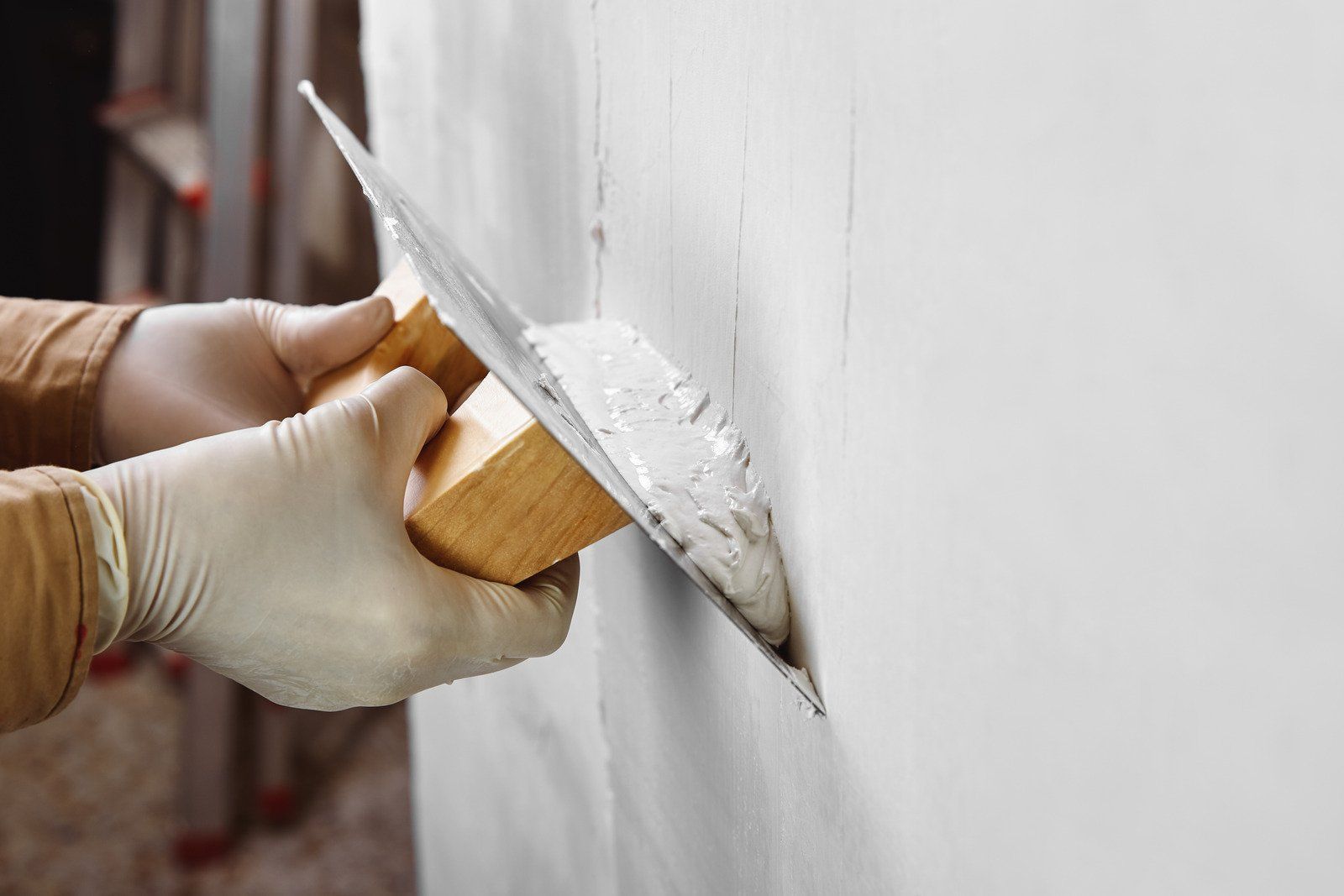 Person using a trowel to apply putty to a wall, filling a crack.