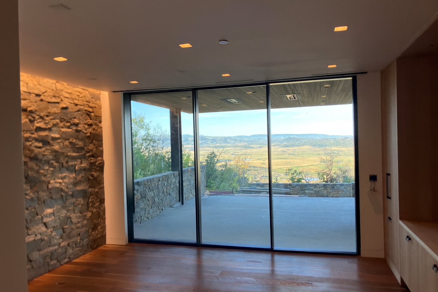 Interior room with large sliding glass doors, stone wall, wood floor, and scenic view.