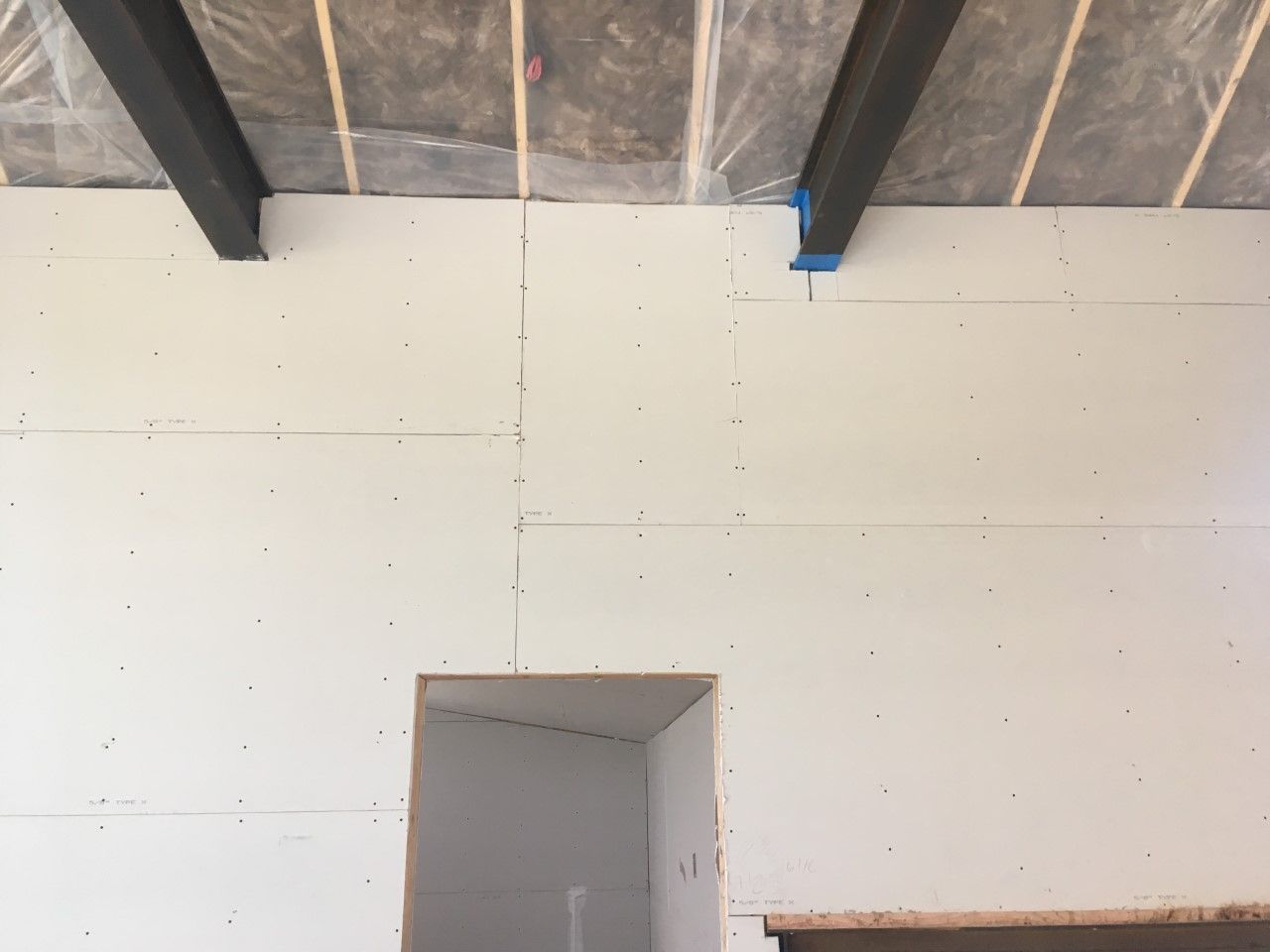 White drywall on interior wall, with exposed beams and a doorway opening.