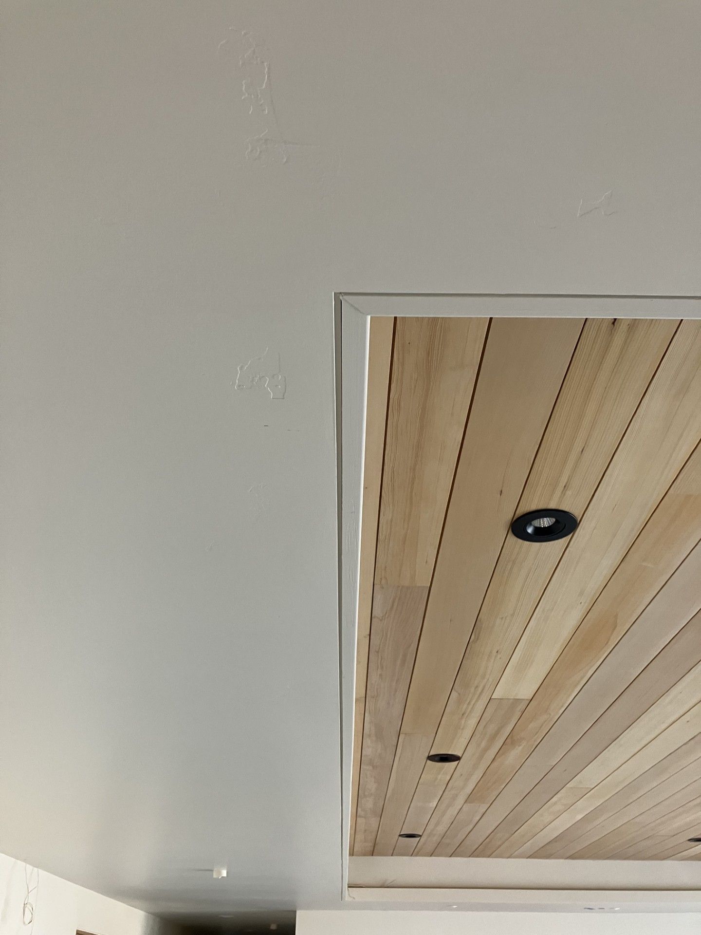 White ceiling meets a wood paneled ceiling with recessed lights, framed by a white border.