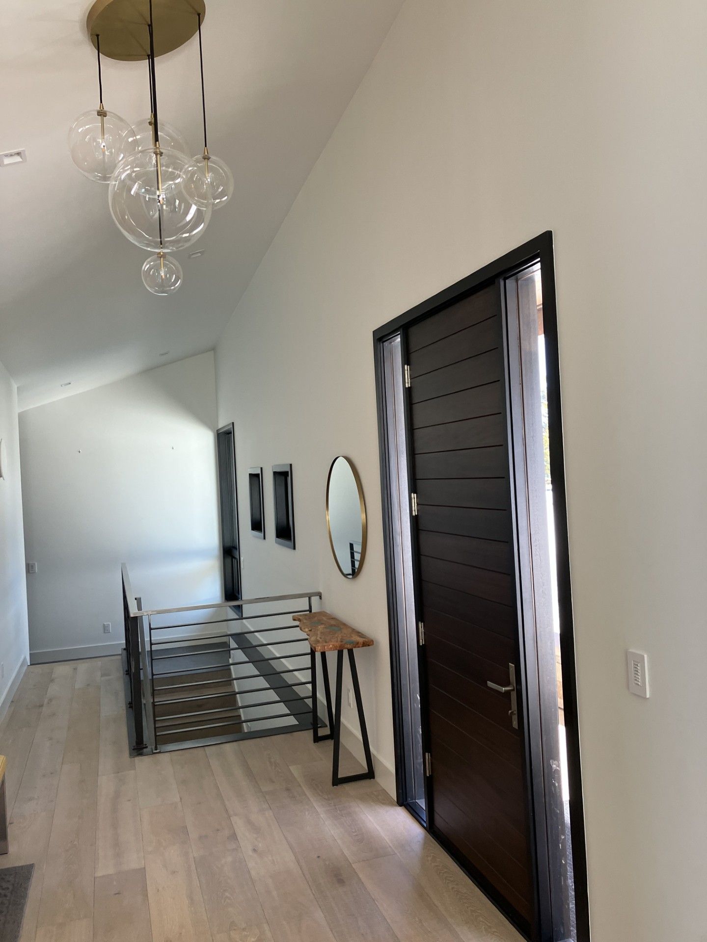 Modern hallway with light wood floor, dark door, and glass globe chandelier.