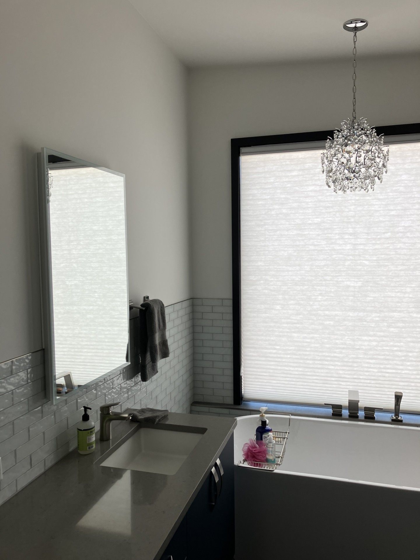 Modern bathroom with a sink, large window, and crystal chandelier.