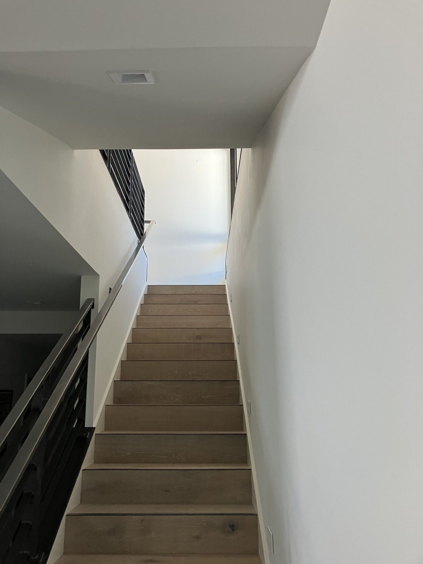 Staircase with light-colored steps, white walls, and a black and steel railing on the left.