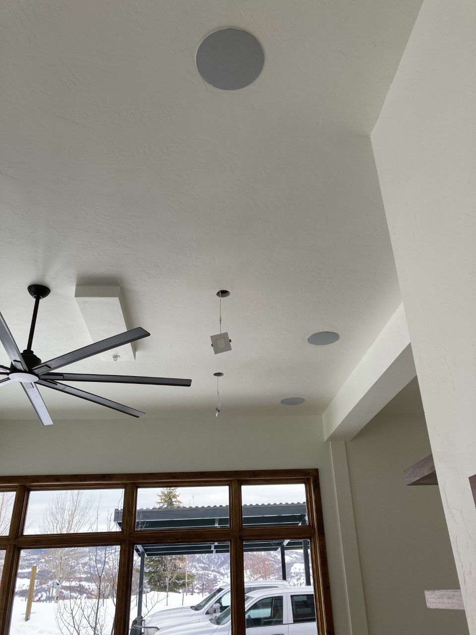 White ceiling with recessed lighting and a ceiling fan. Large windows and a vehicle visible outside.