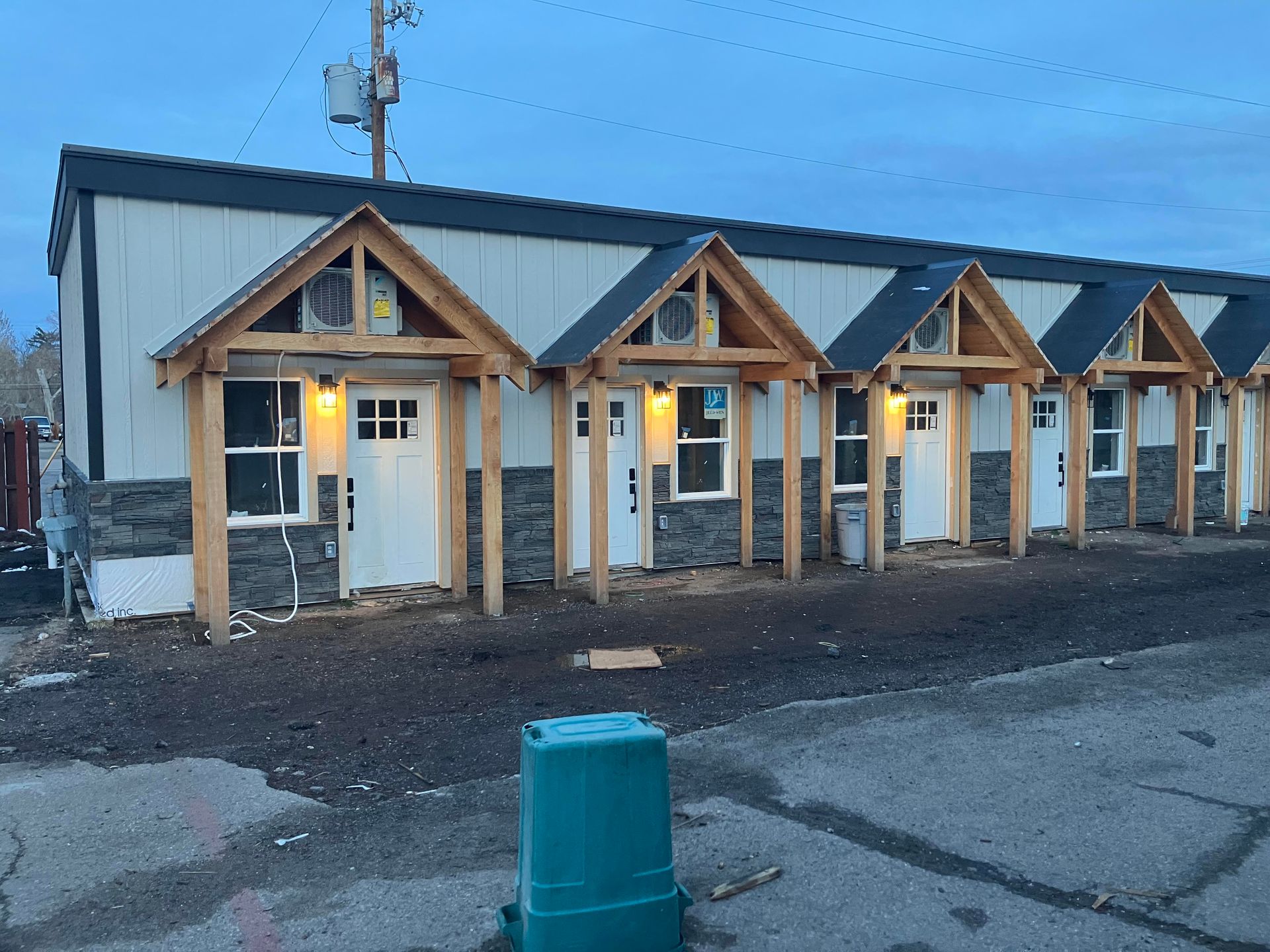 Row of small buildings with gabled entryways, white doors, and stone accents. Gray sky.