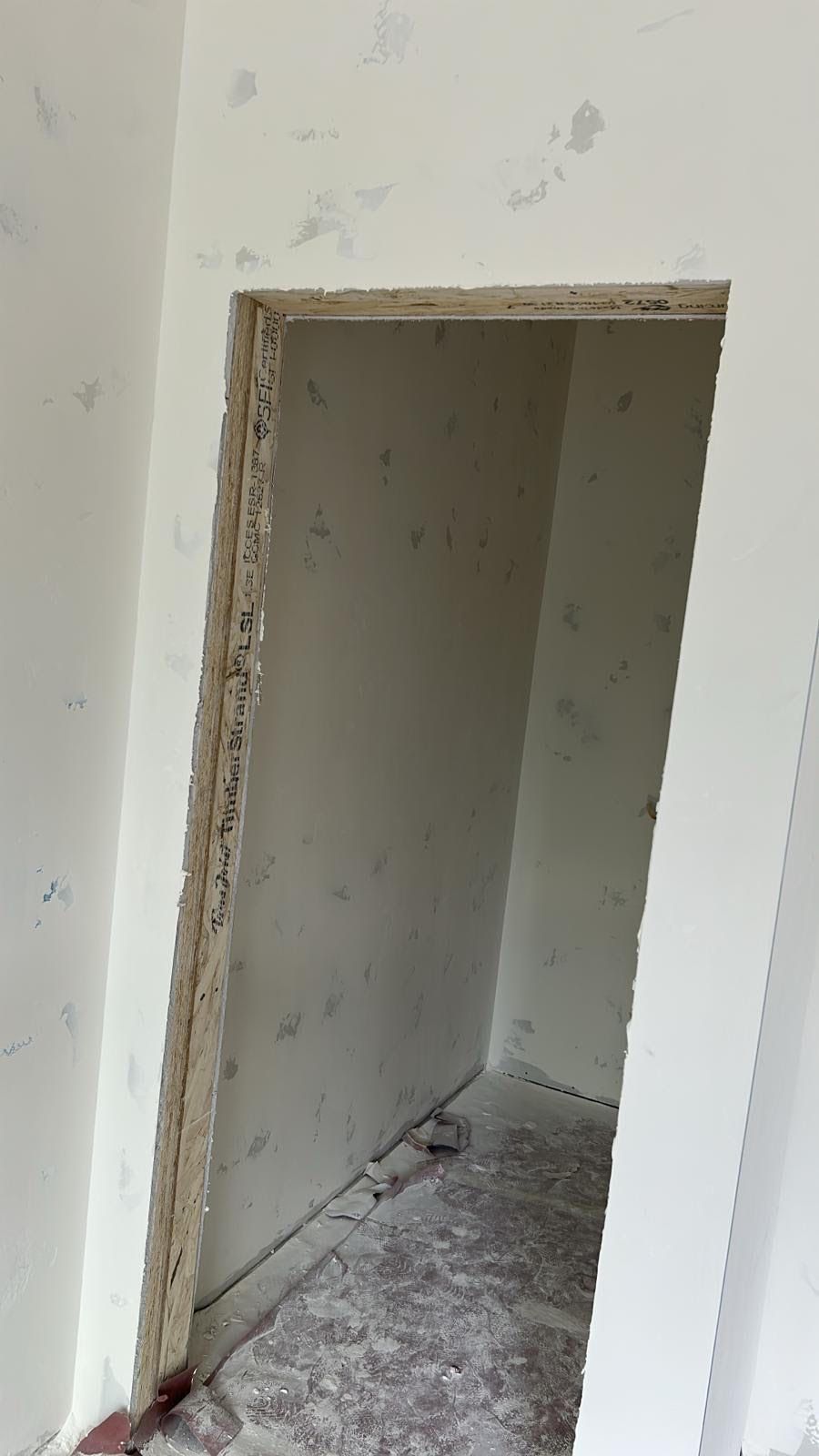 Unfinished doorway in a room. The door frame is made of light-colored particleboard, and the walls are painted white.