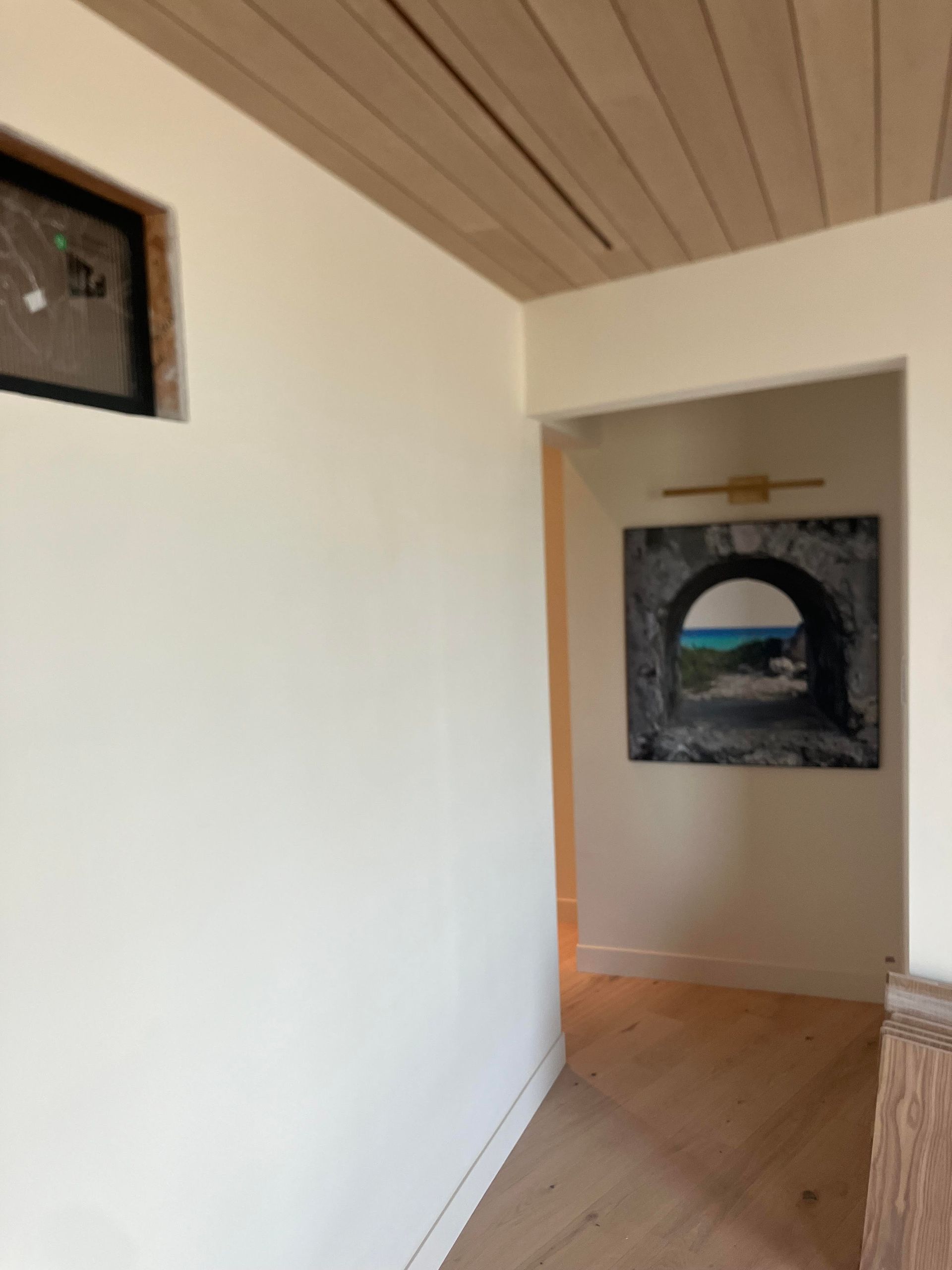 Hallway with white walls, wood ceiling, and framed art.