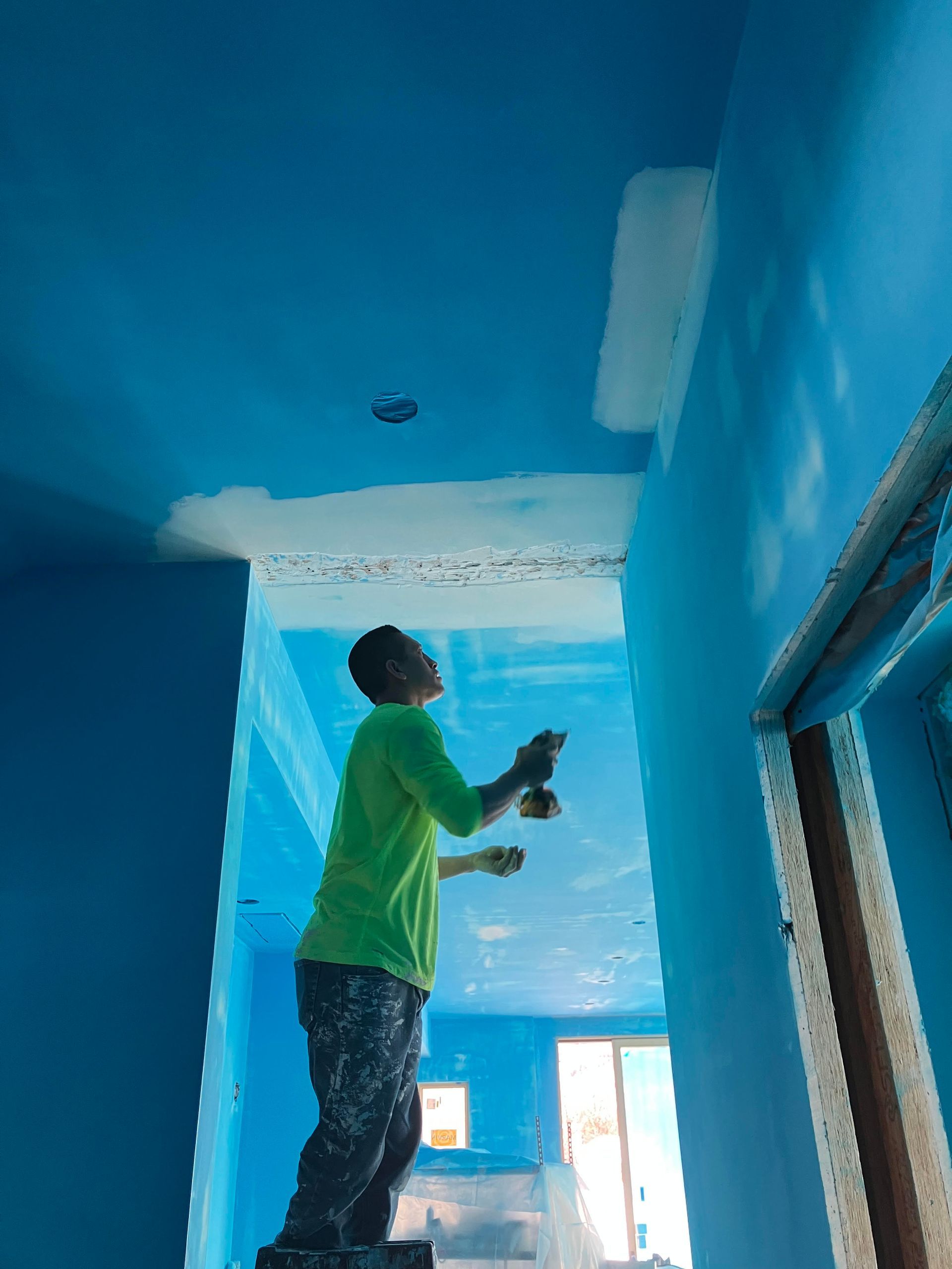 Person painting a ceiling blue, standing on a step stool.