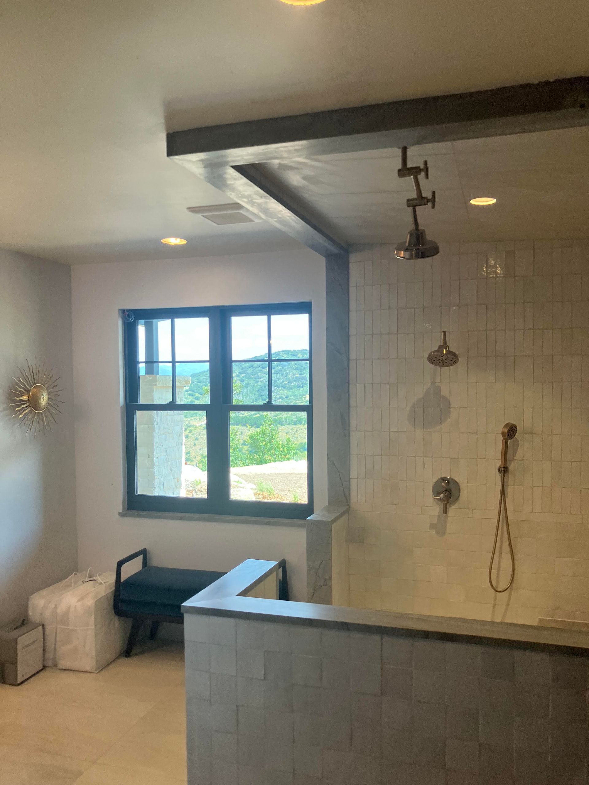 Bathroom with shower and window overlooking a green landscape. Gray and white tiles and fixtures.
