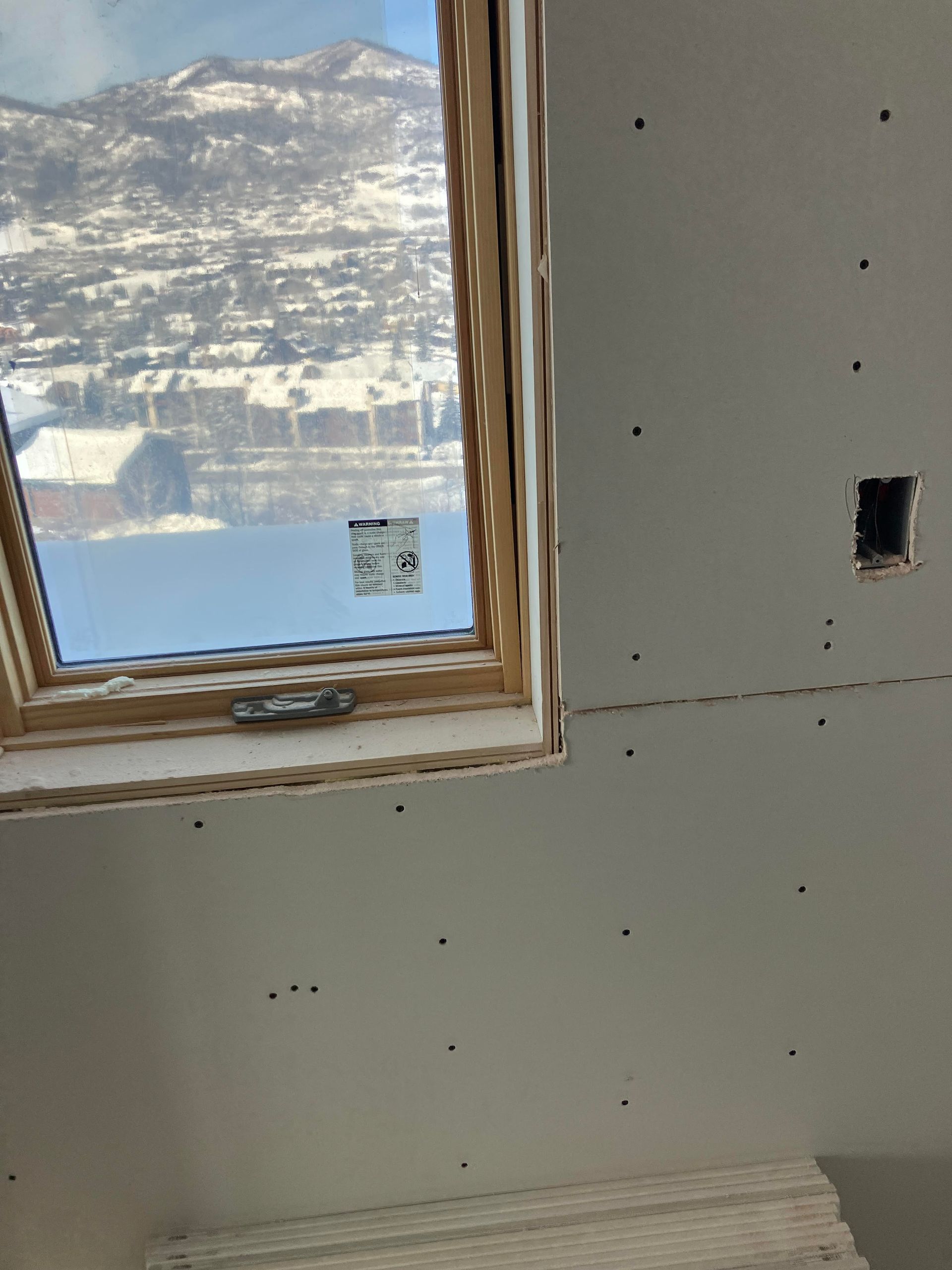 Interior shot of a skylight in a room under construction with a mountain view outside. Drywall and electrical outlet visible.
