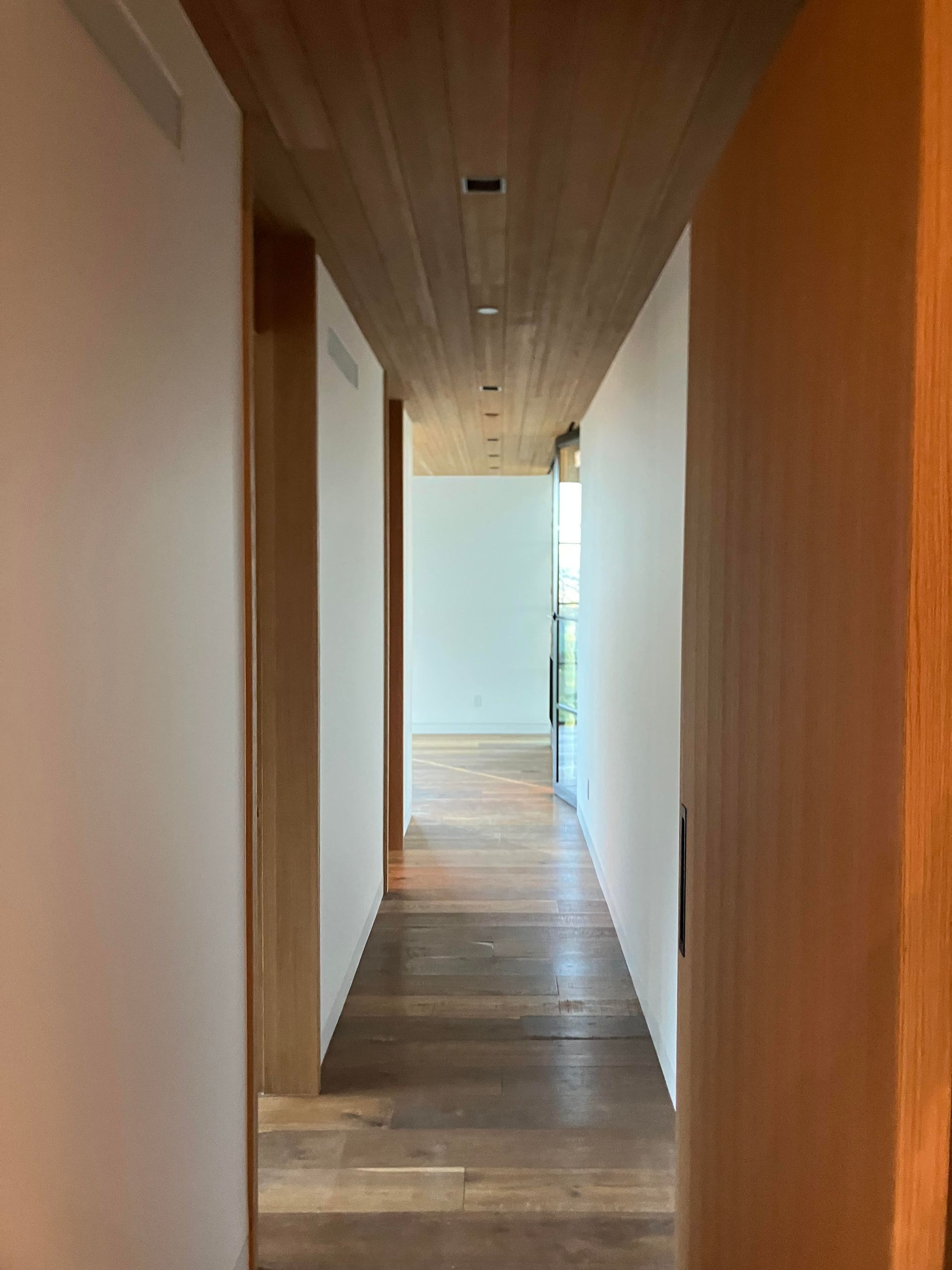 Long hallway with wood ceiling, floors and trim, white walls.