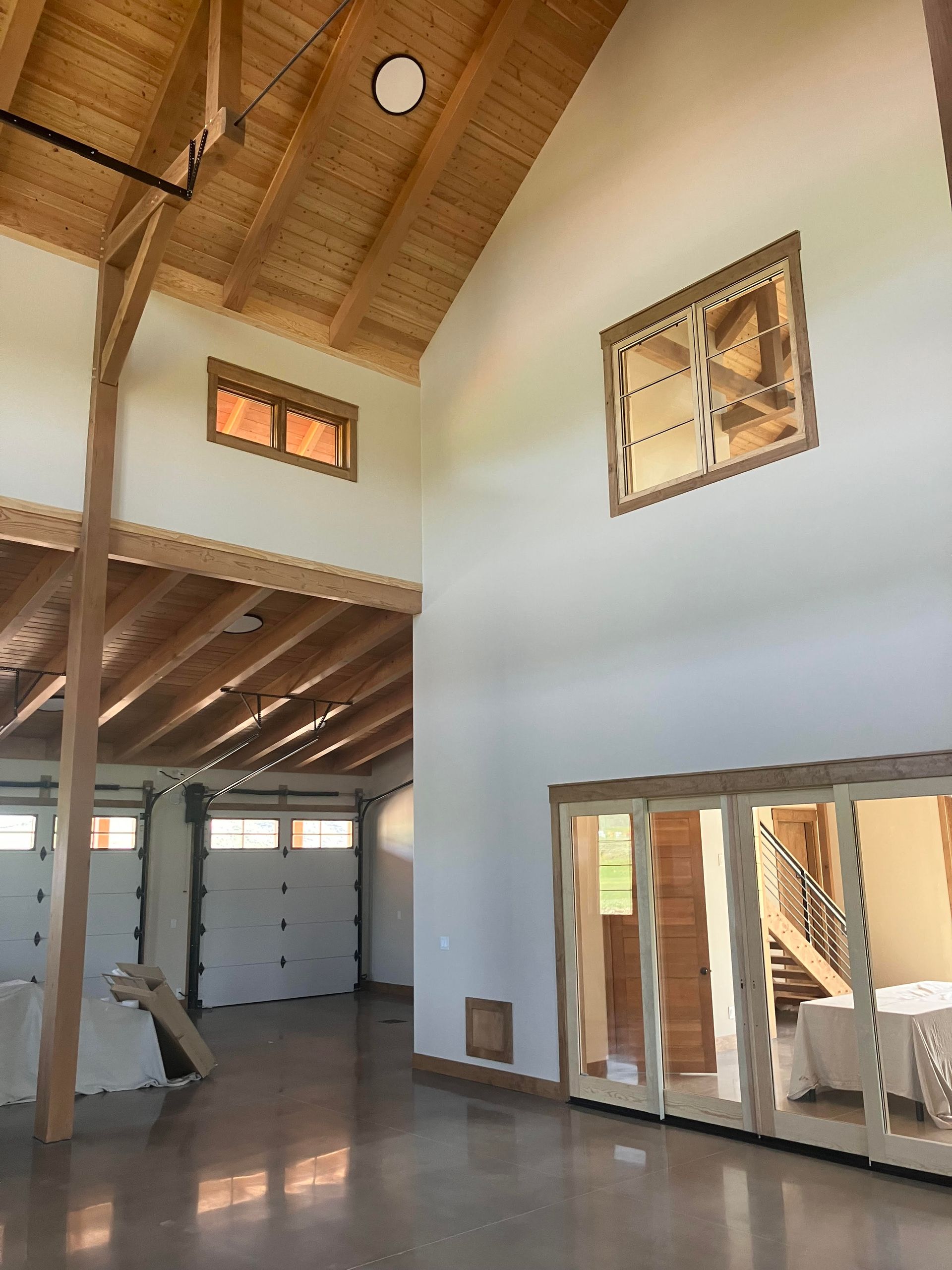Interior of a building with high ceilings, wood beams, and large windows. Concrete floor and white walls.