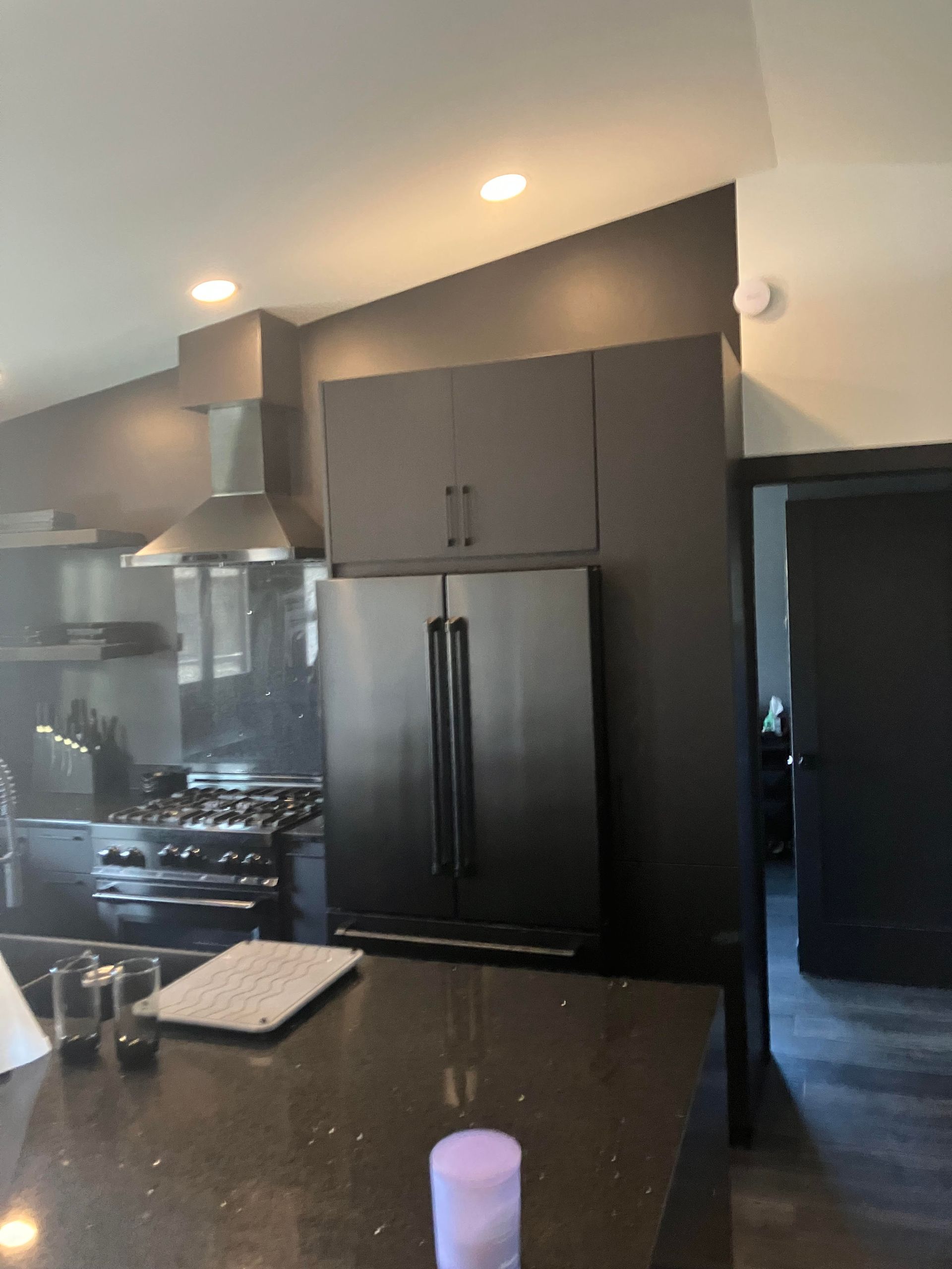 Black kitchen with stainless steel refrigerator, black cabinetry, and black countertop.