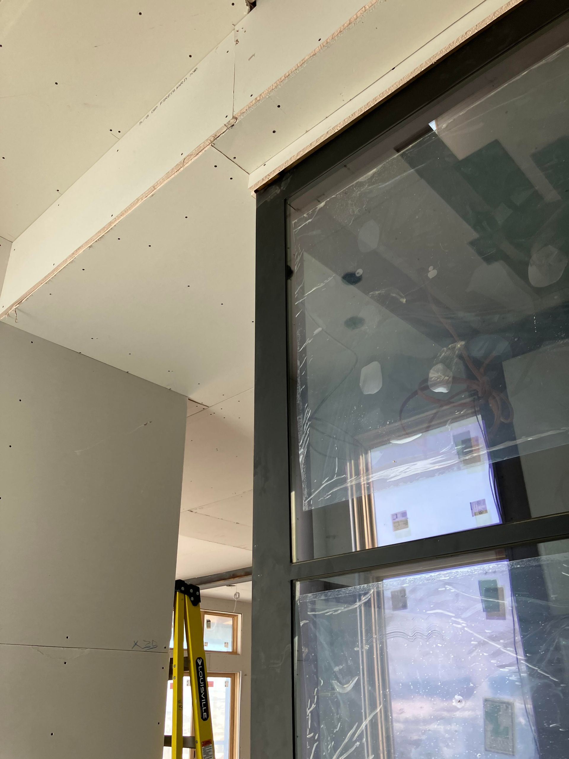 Interior view of a window, covered in plastic, with unfinished drywall surrounding it.