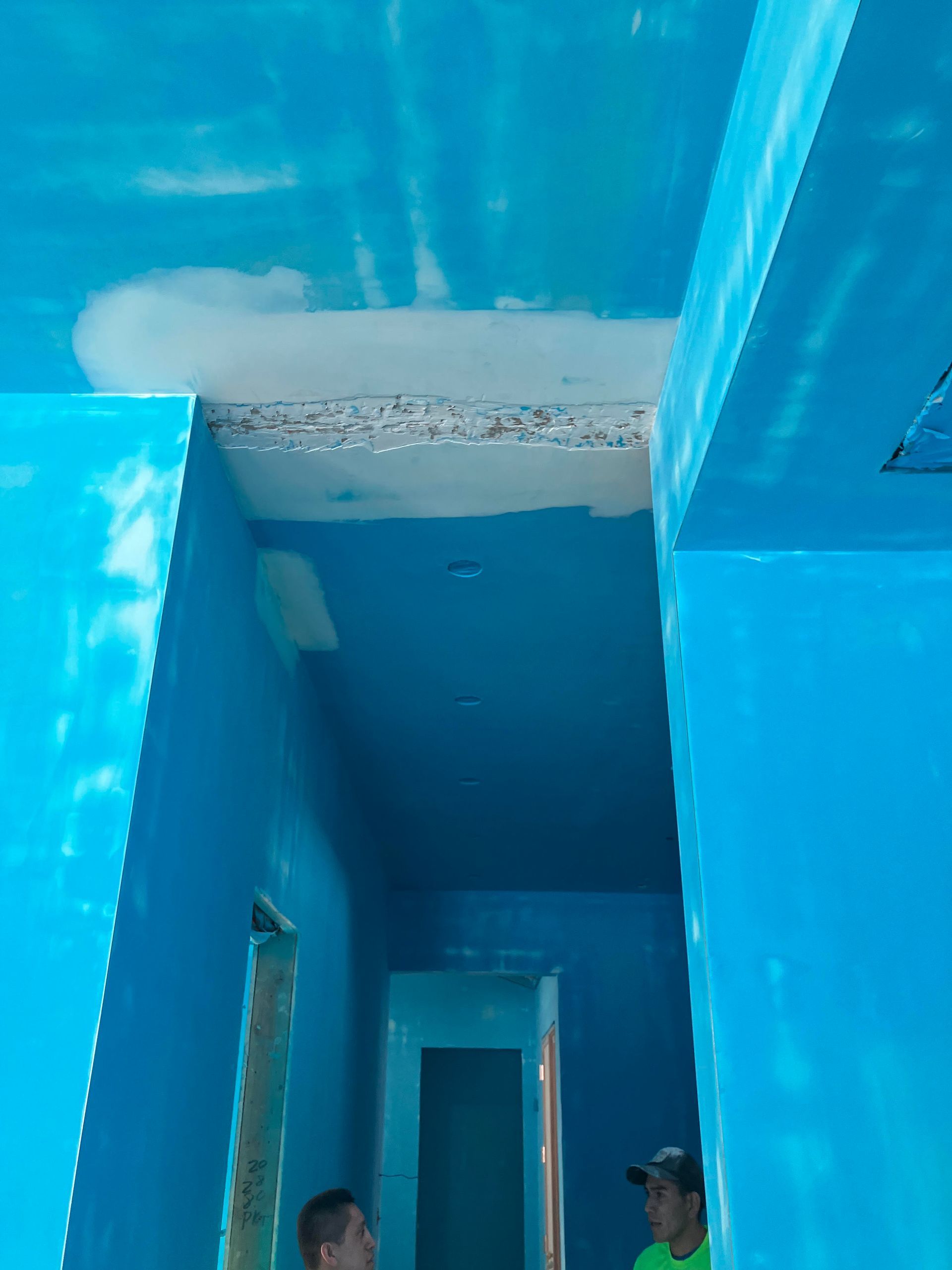 Blue-painted interior hallway with workers looking at a ceiling with visible damage.