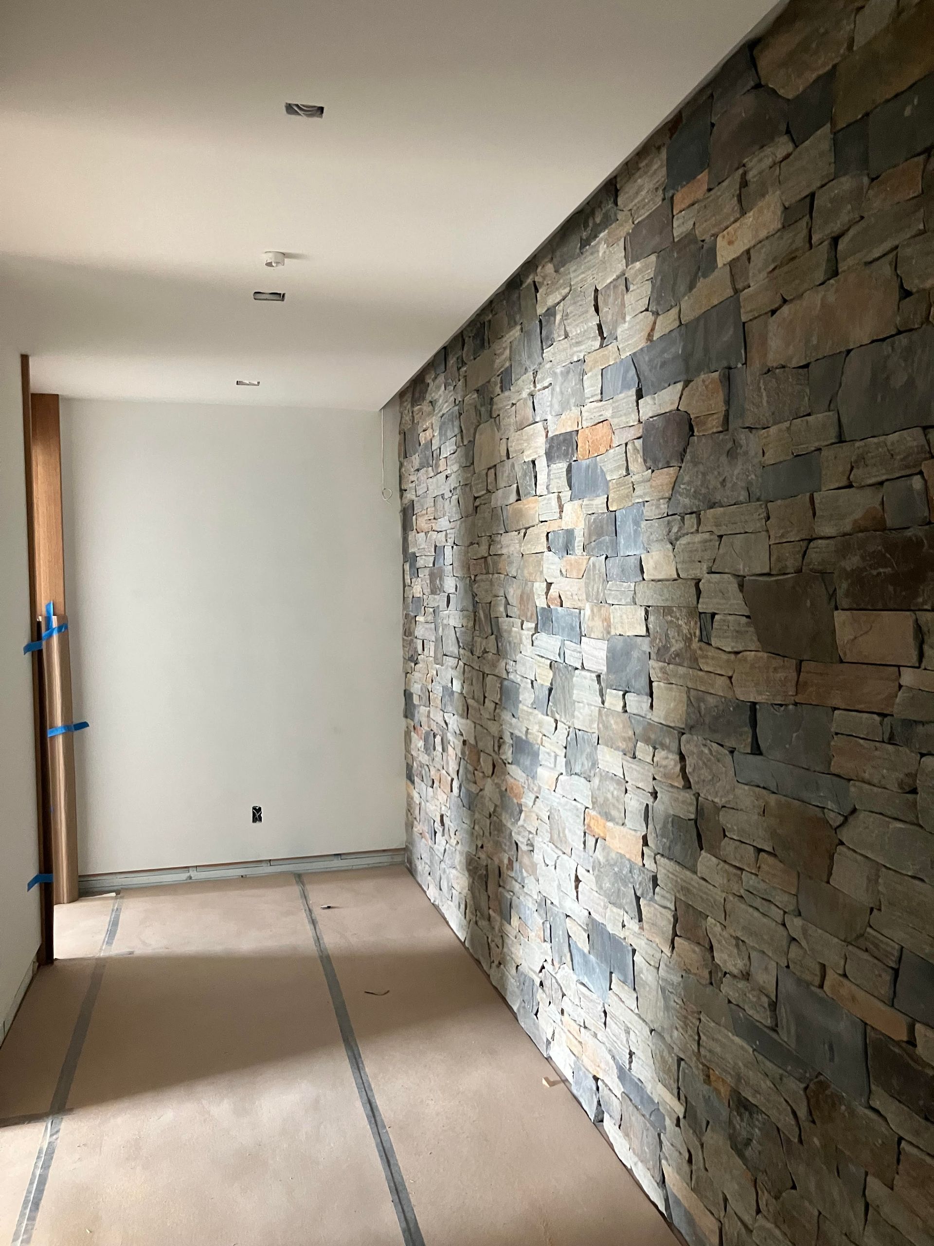 Interior hallway with a stone accent wall, white walls, and unfinished flooring.