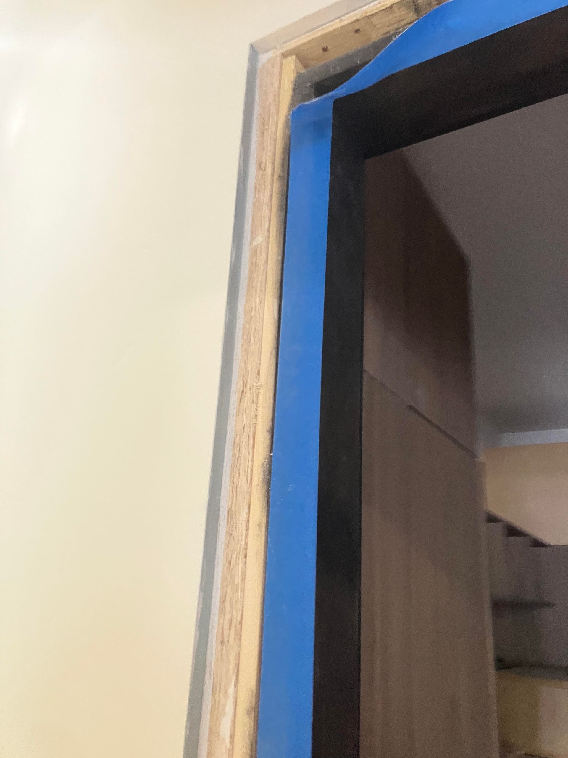 Blue tape lines a door frame. Light wood, dark door, beige wall visible.