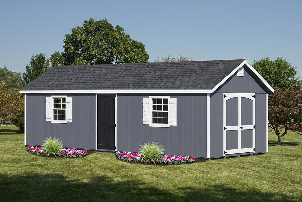 Gray shed with white trim, two windows with shutters, and double doors; set in a grassy yard.