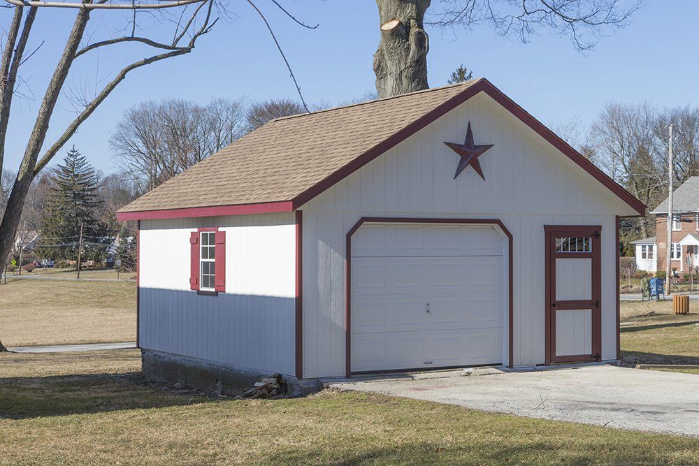 White garage with red trim, brown roof, and a red star on the front, set on a grassy lawn.