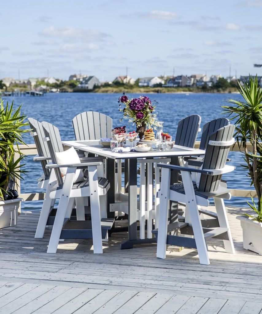 Outdoor dining set with square table and six chairs on a dock by water.