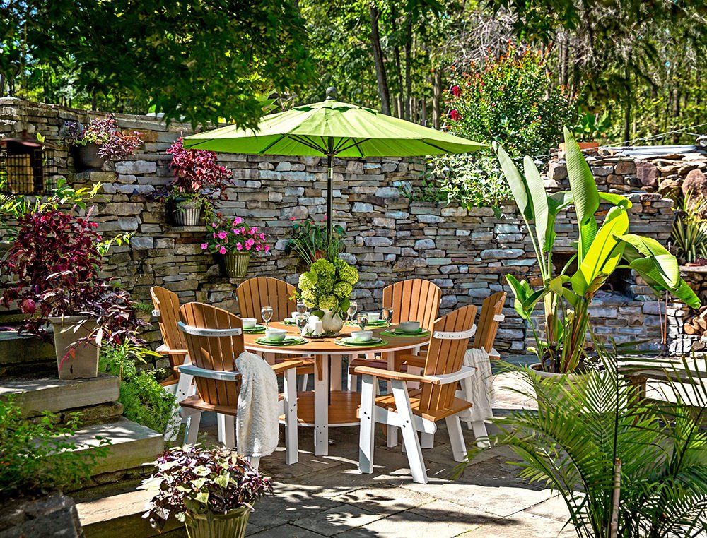 Outdoor dining set with umbrella, surrounded by lush greenery and a stone wall.