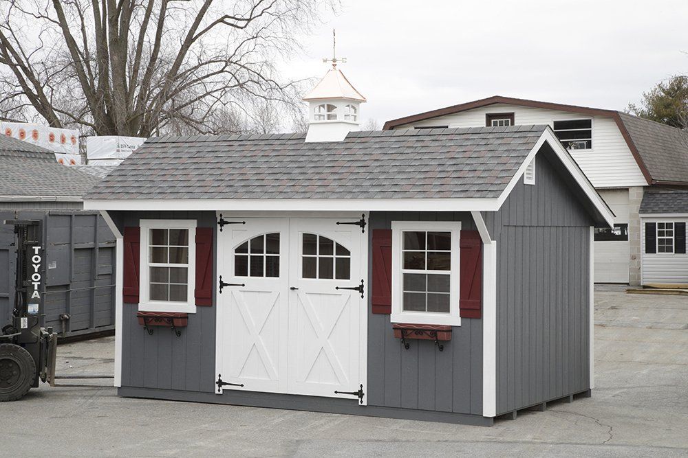 Gray shed with white doors and trim, windows with red accents, and a gray roof.