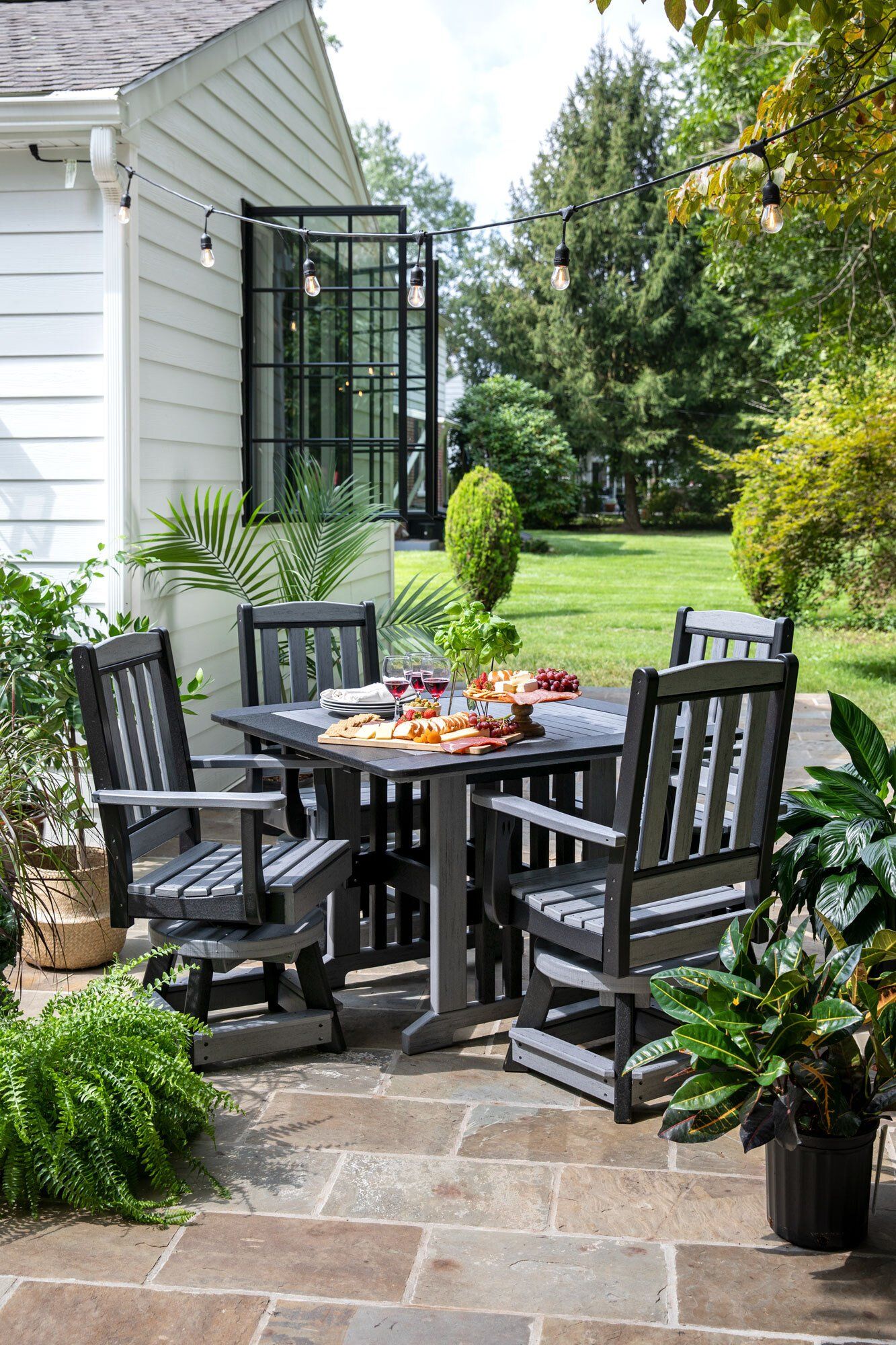 Outdoor dining set on a patio near a white building and greenery.