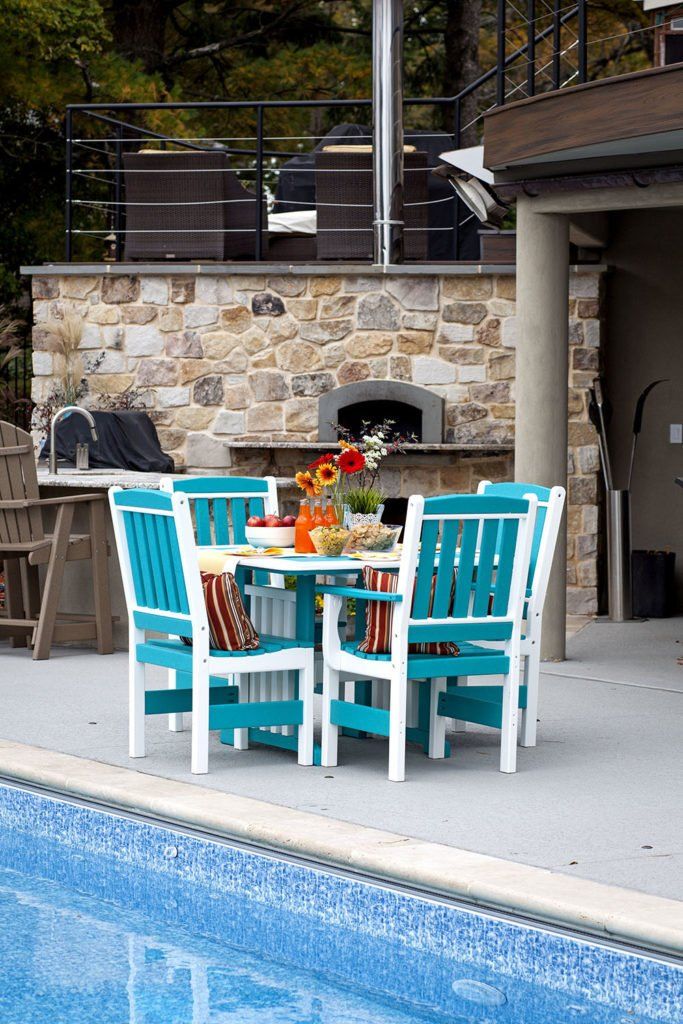 Teal and white outdoor dining set by a pool with stone oven and flowers.