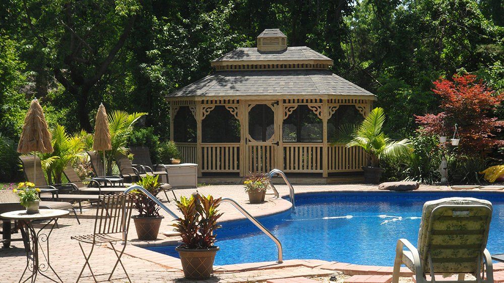 Poolside gazebo with pool, patio furniture, and potted plants in a sunny outdoor setting.