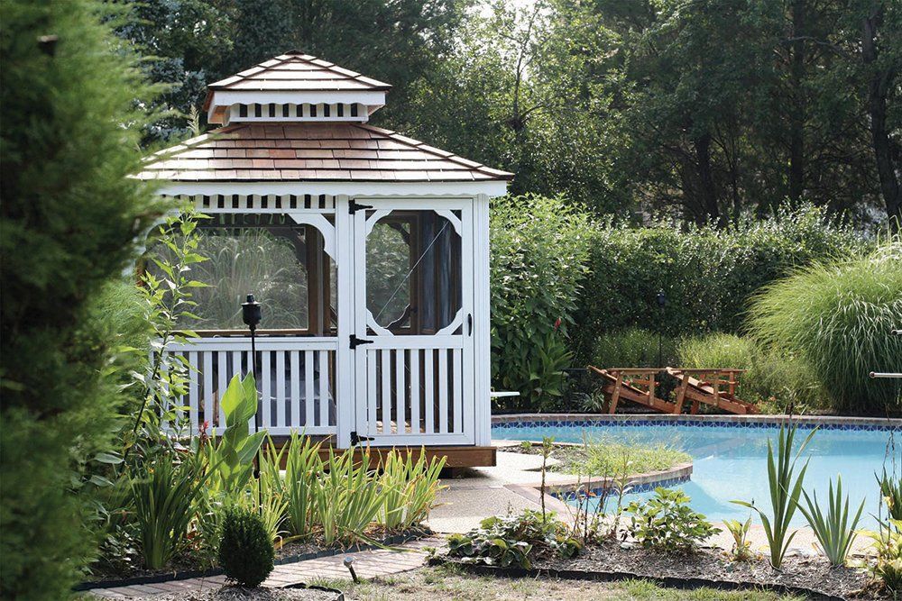 White gazebo by a pool with surrounding landscaping.