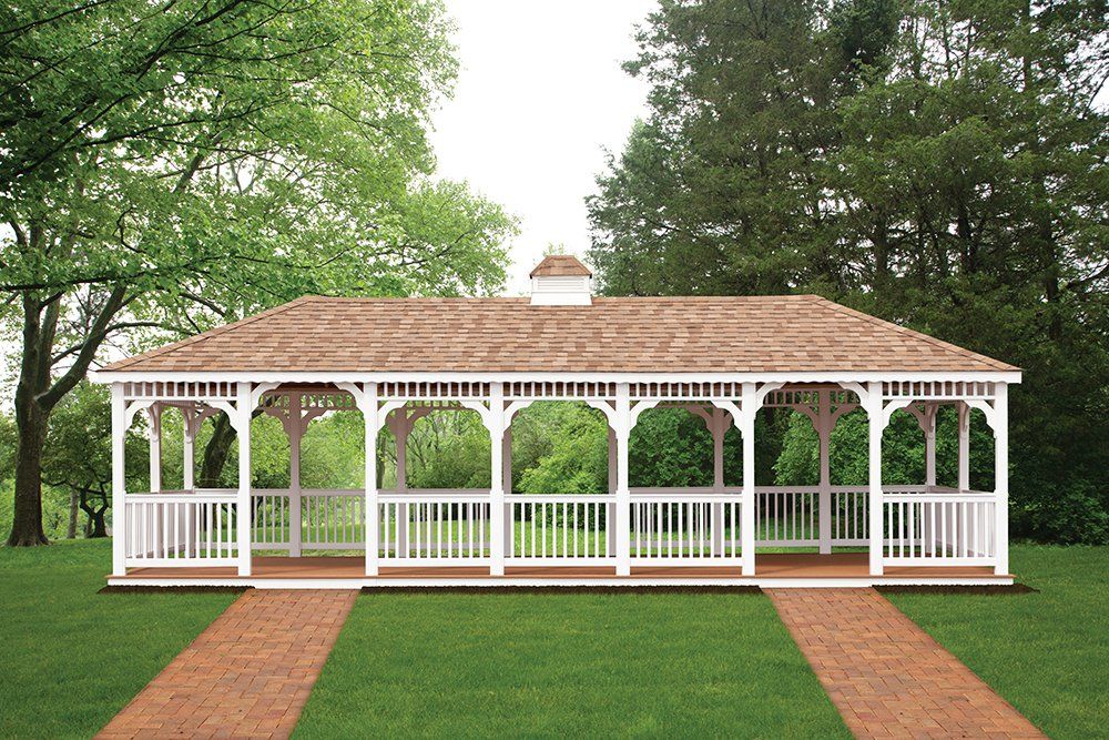 White gazebo with brown roof in a green grassy area with brick pathways and trees in the background.