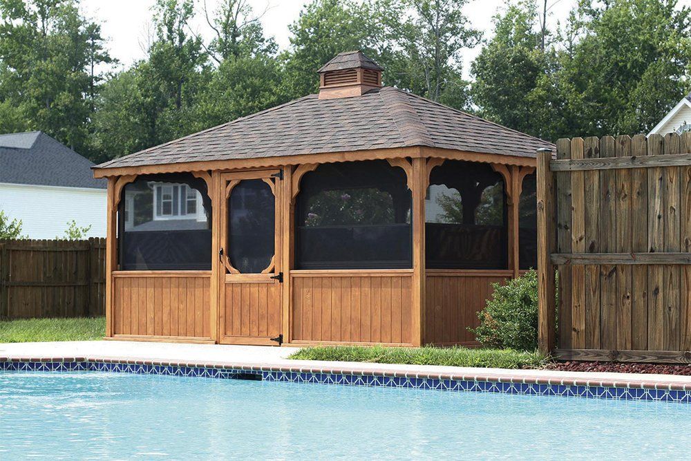 Wooden gazebo with screened windows by a pool.