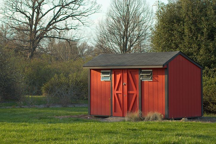 A rustic backyard shed made of red wood panels, showcasing storage shed installation services