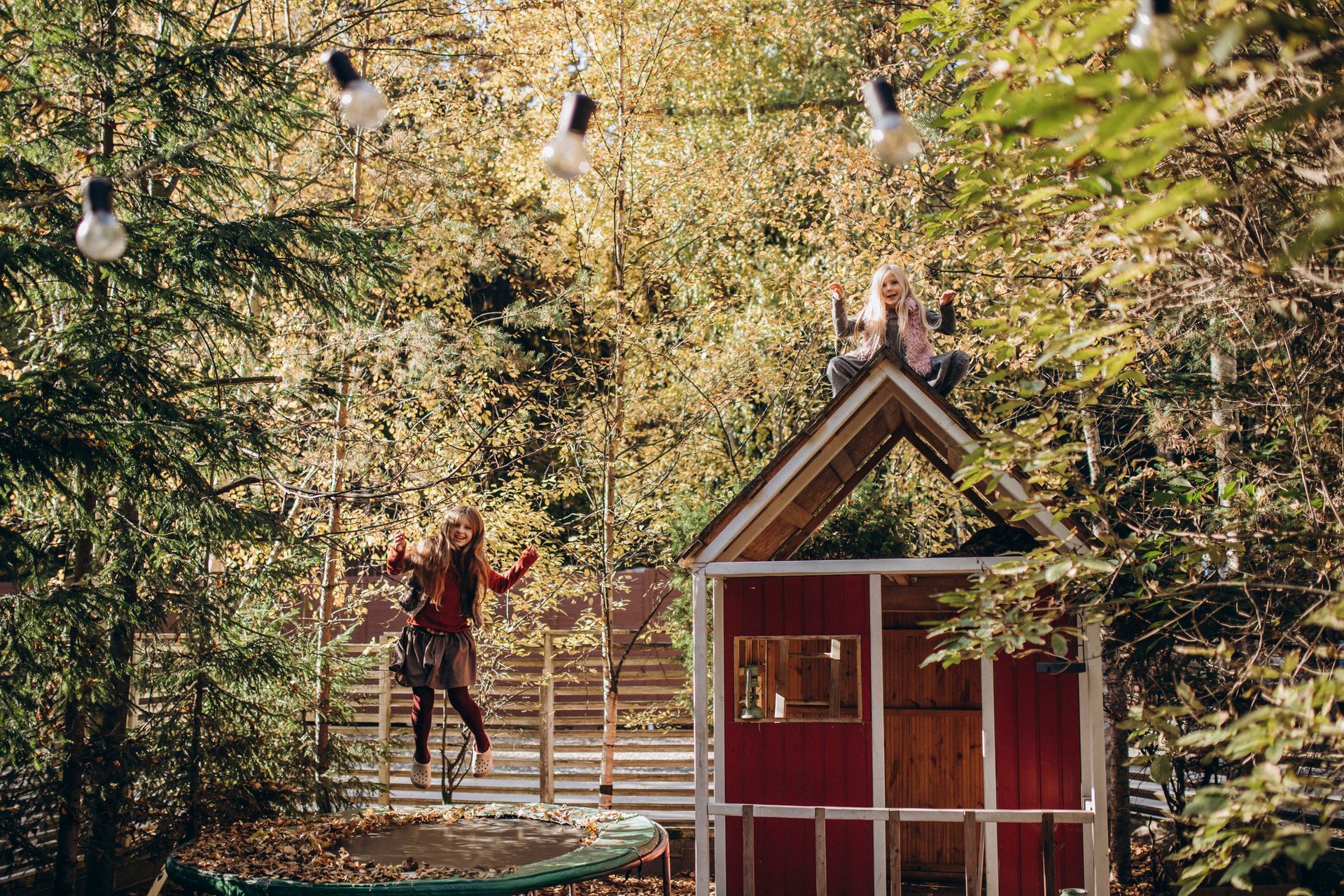 Girl jumping on a trampoline with friend sitting on top of a shed.